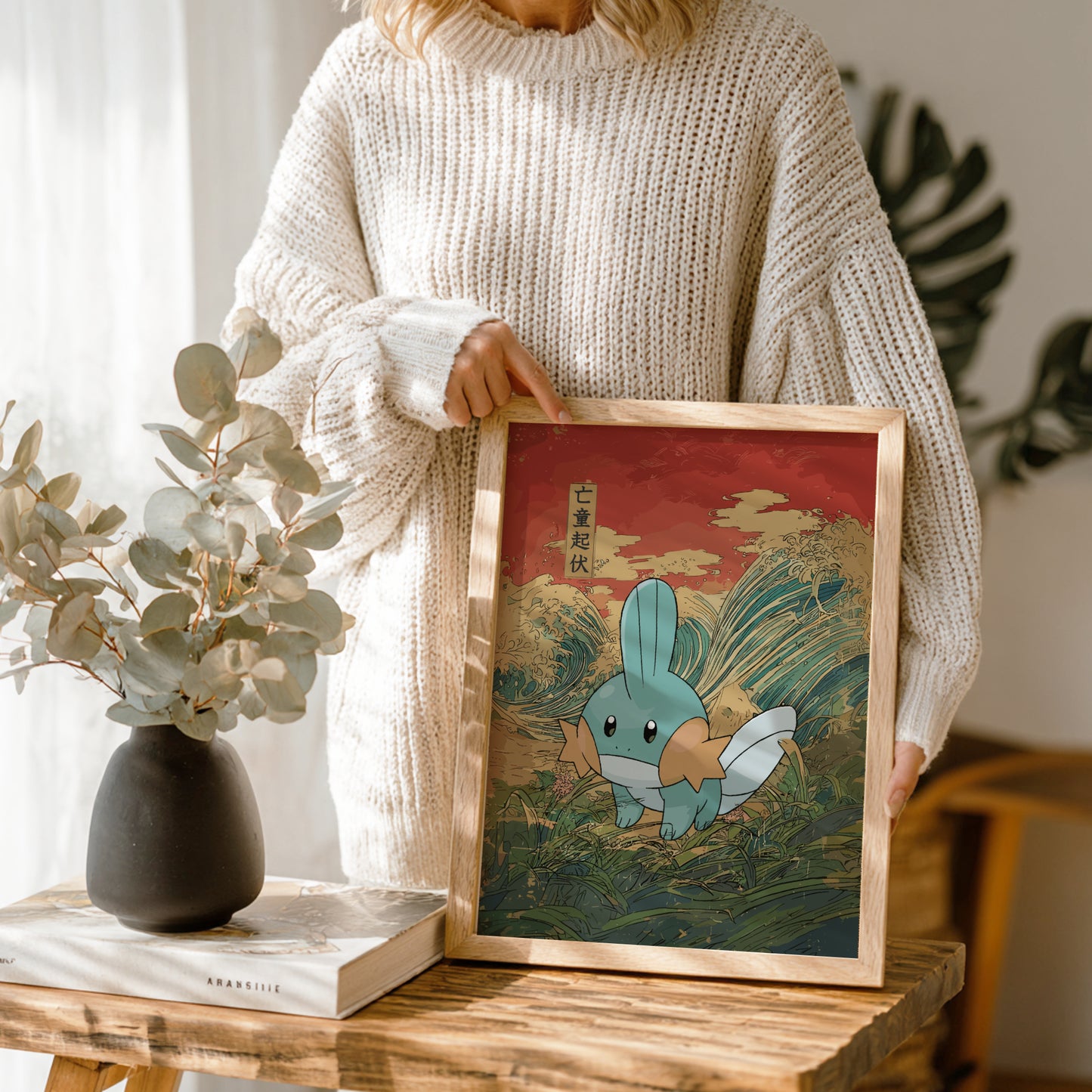 Person holding a framed illustration of Mudkip Pokemon with a natural setting