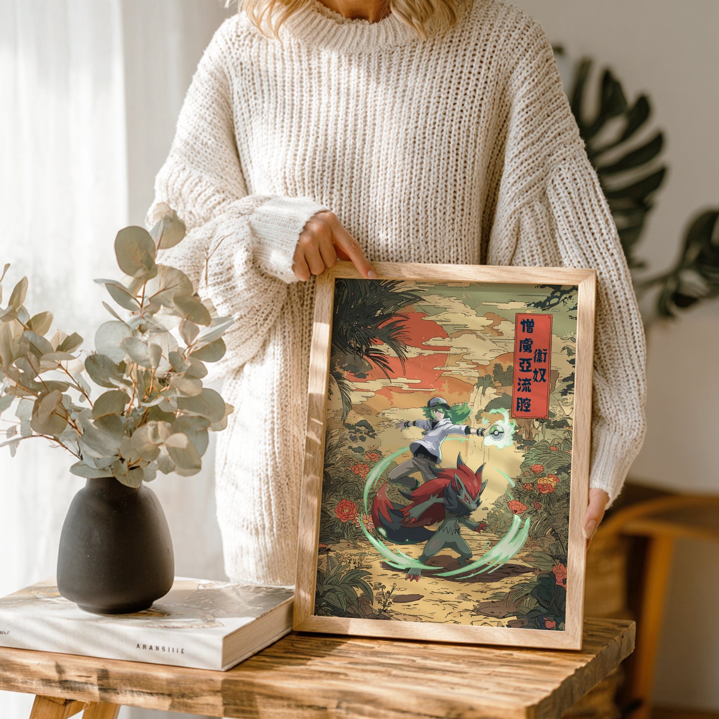 Person holding a framed artwork of N and Zoroark Pokemon on a wooden table with a vase and book in the background.