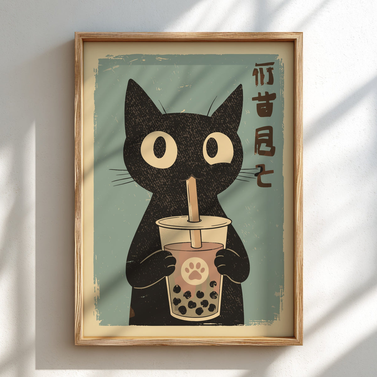 A framed art print featuring a black cat holding a bubble tea cup with a straw, set against a muted teal background with vertical brown Japanese characters. The print is housed in a light wood frame and displayed on a white wall with soft diagonal shadows.