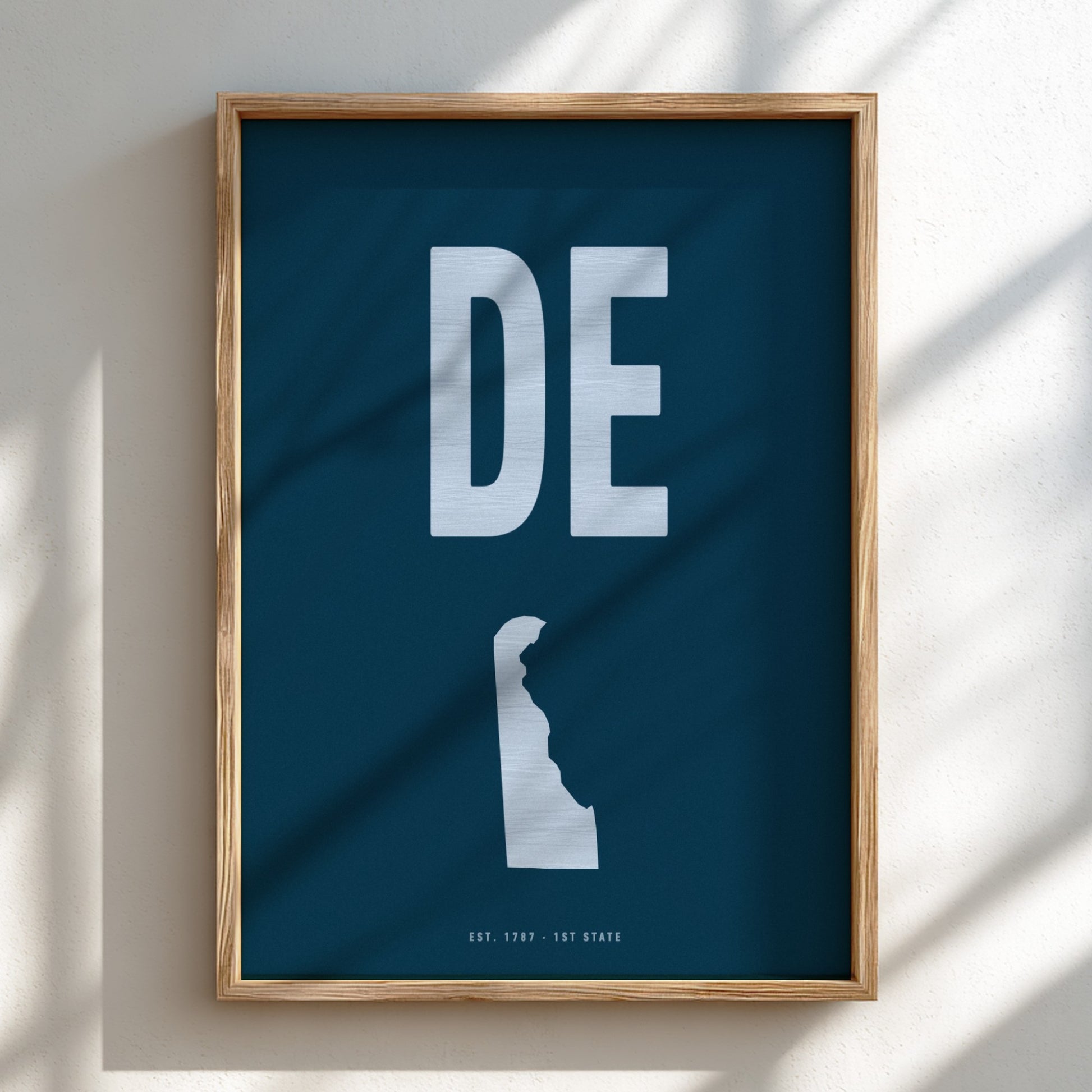 Framed poster with 'DE' on a blue background, featuring a silhouette of a state.