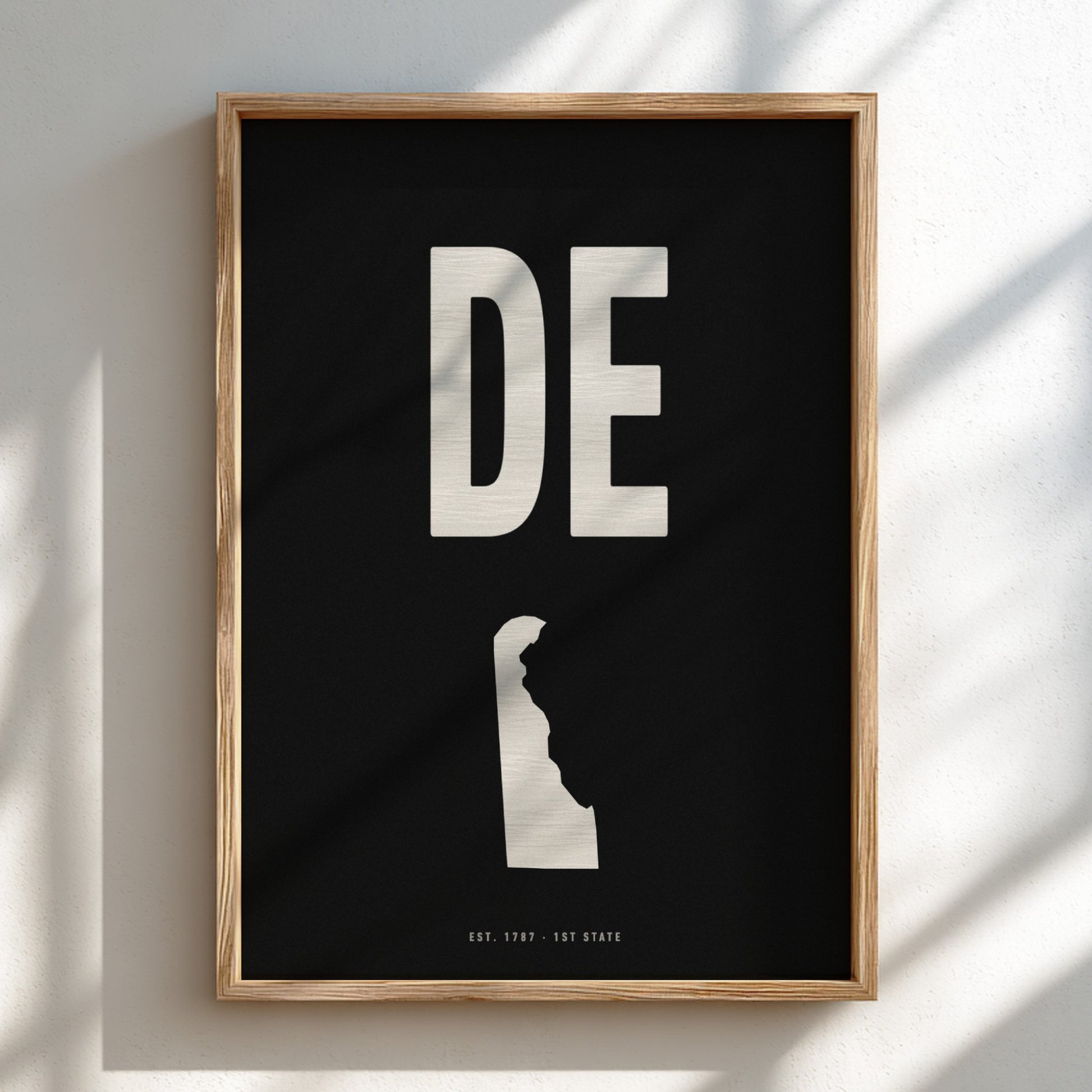 Framed artwork with 'DE' and silhouette of Delaware on a black background