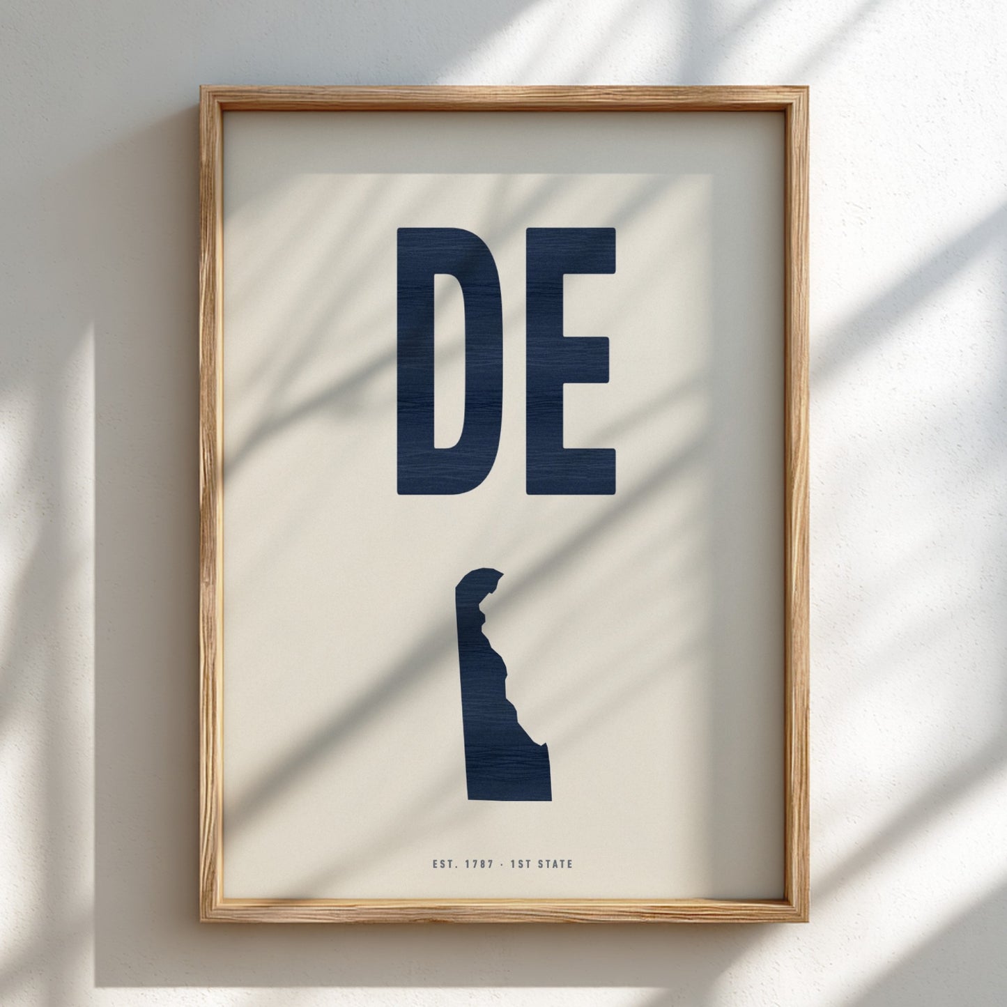 Framed artwork with 'DE' in navy on a light background