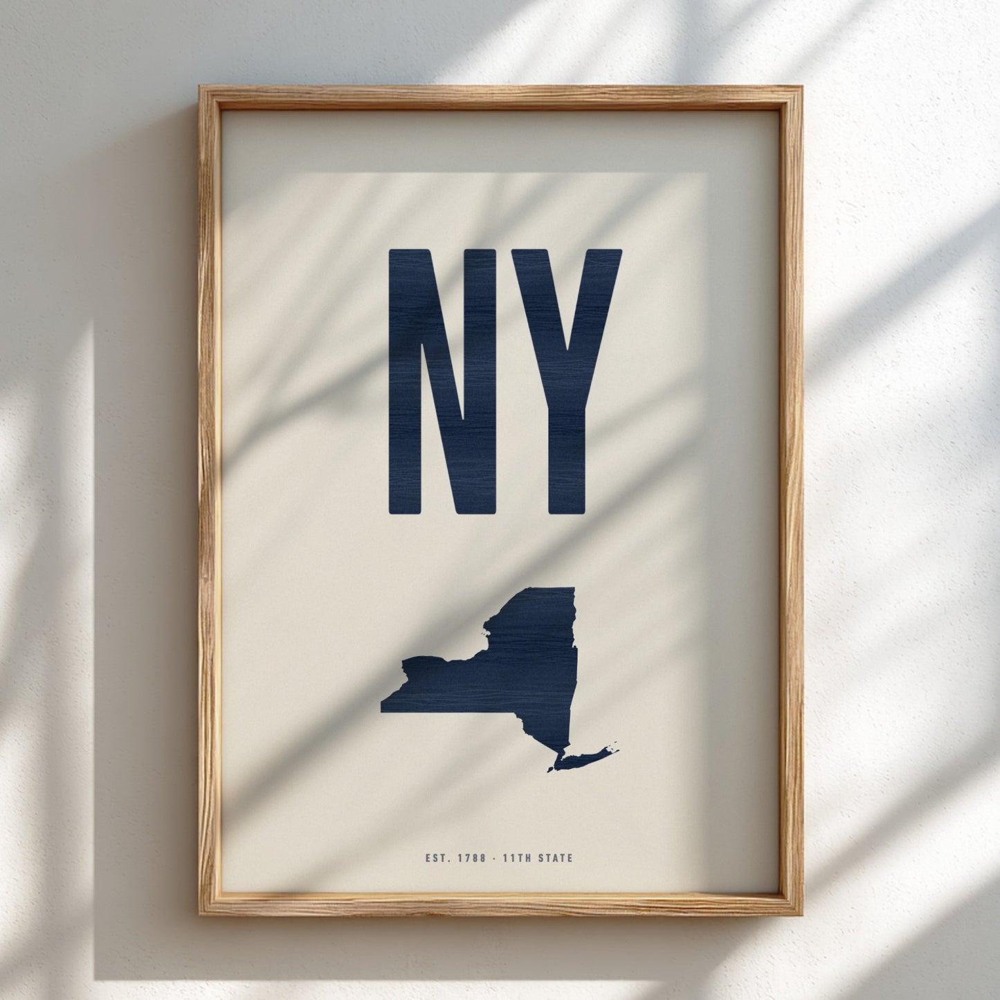 Framed artwork of a navy blue 'NY' and map of New York on a beige background