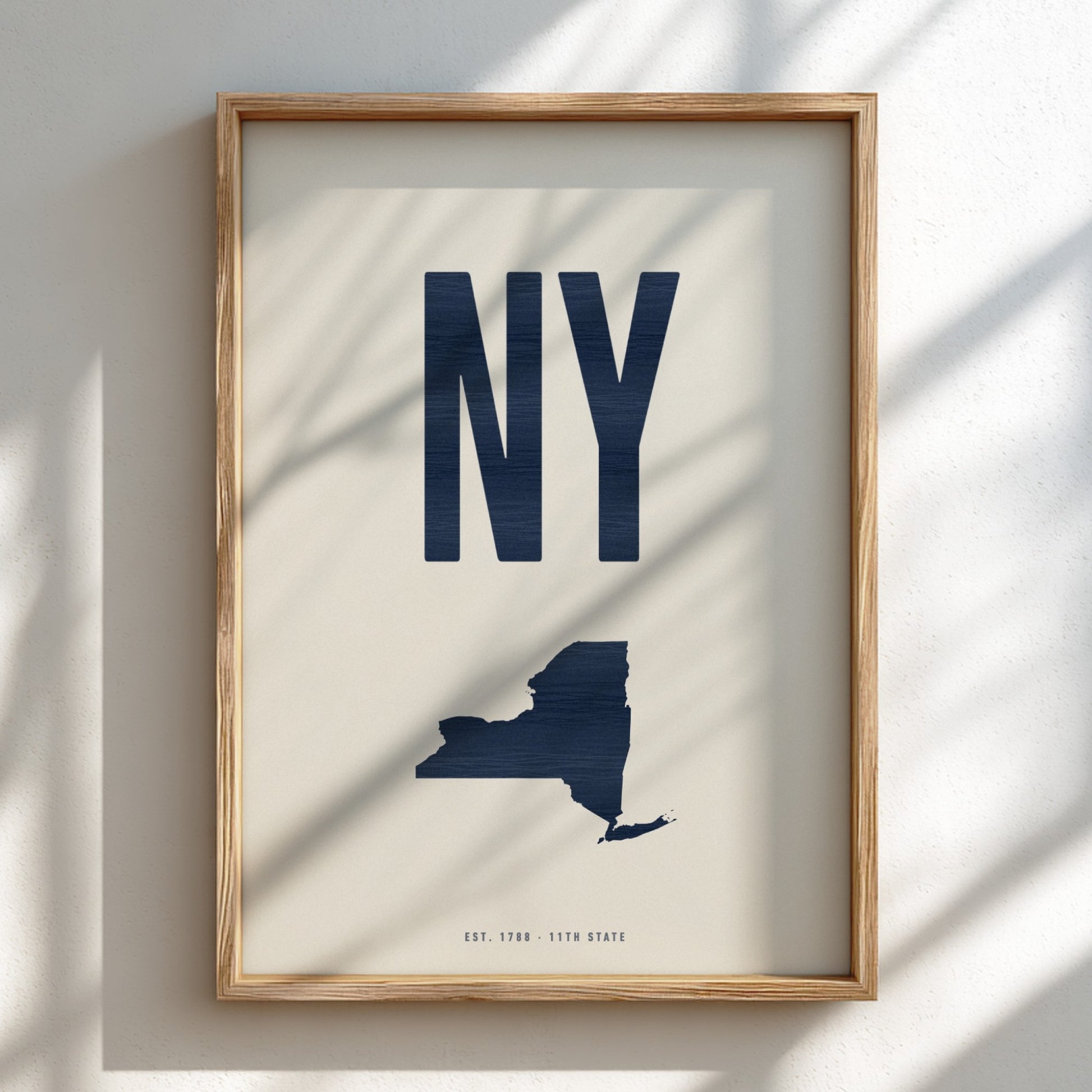 Framed artwork of a navy blue 'NY' and map of New York on a beige background