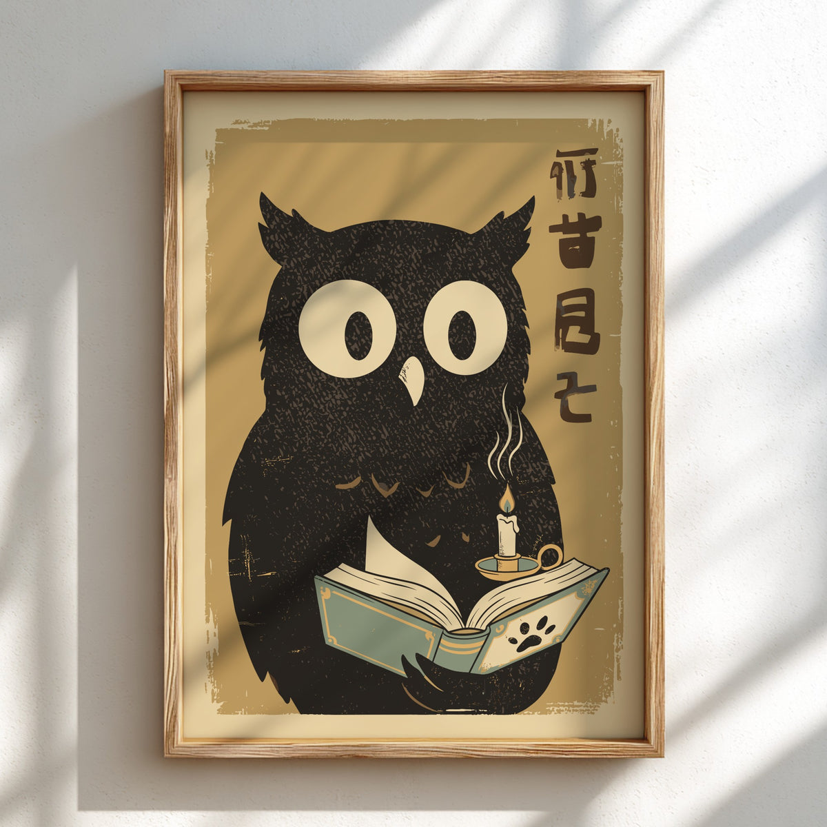 A framed art print featuring a black owl illustration with large white eyes, reading a book with a candle on a warm beige background, hung on a white wall with soft diagonal shadows.