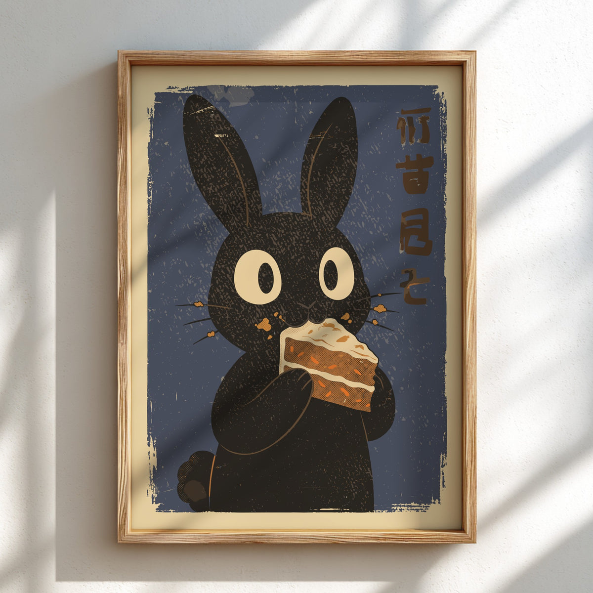 A framed art print featuring a stylized black rabbit holding a slice of cake against a dark blue background with Japanese characters, mounted on a light wall with soft diagonal shadows.
