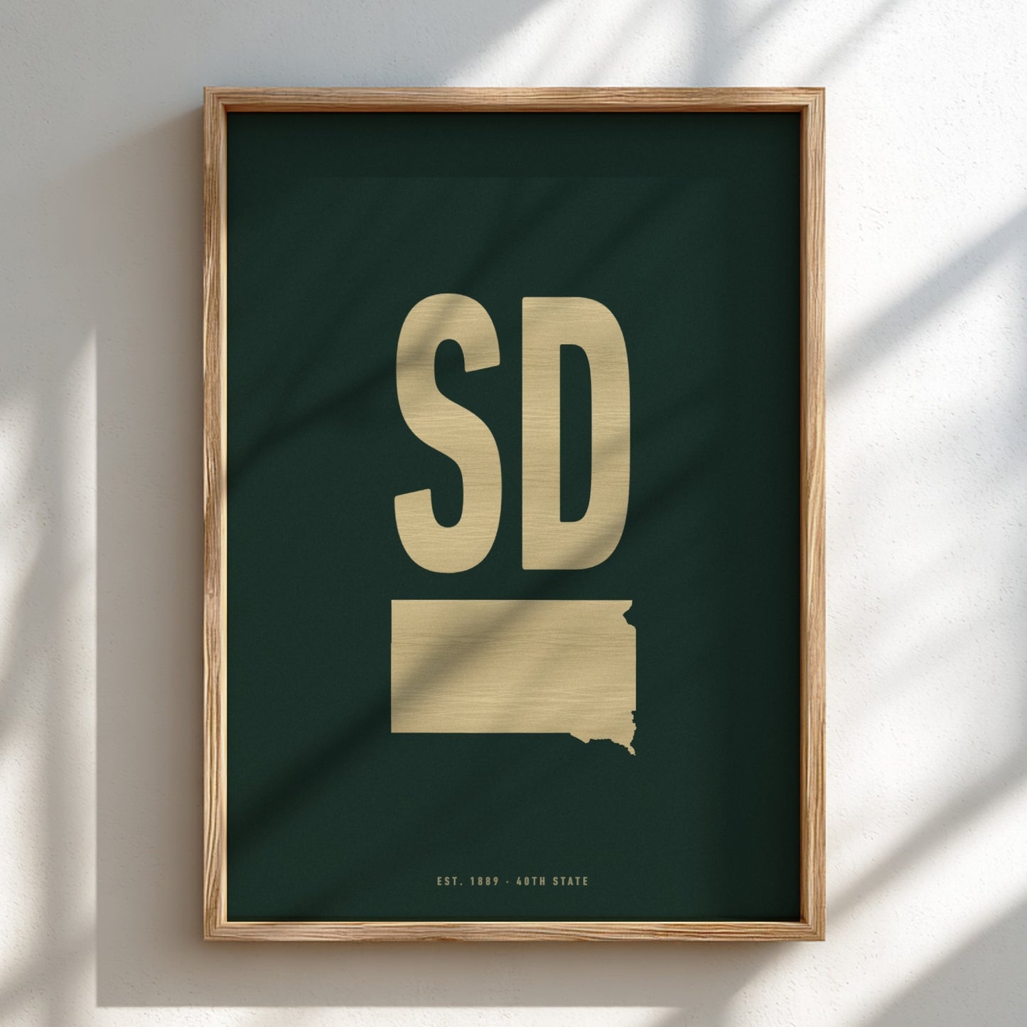 Framed artwork with 'SD' and a map outline of South Dakota on a dark green background.