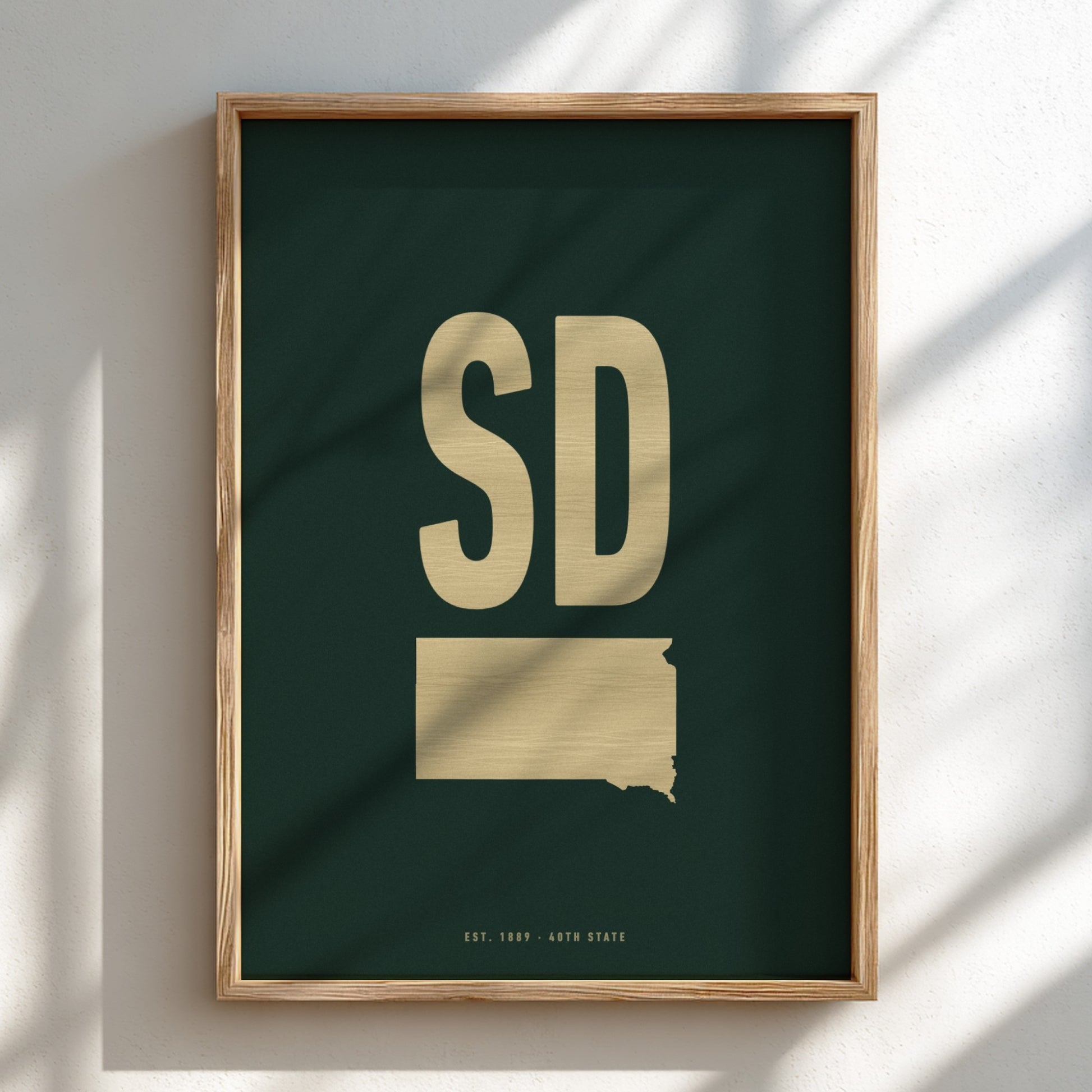 Framed artwork with 'SD' and a map outline of South Dakota on a dark green background.