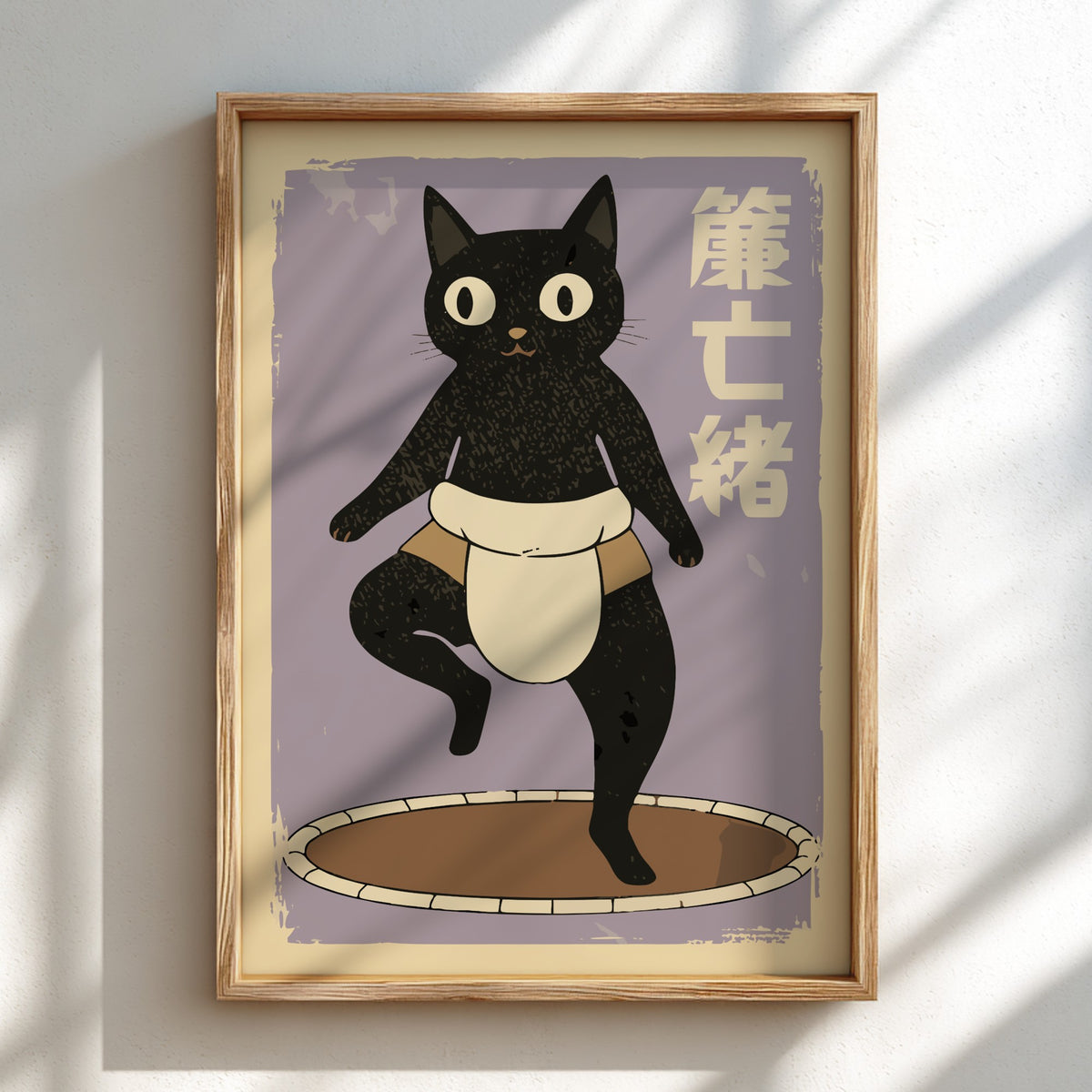 A framed art print featuring a black cat character wearing a white and tan waist cloth, standing on a circular platform against a muted lavender background with vertical Japanese characters. The print is housed in a light wood frame and displayed on a white wall with soft diagonal shadows.