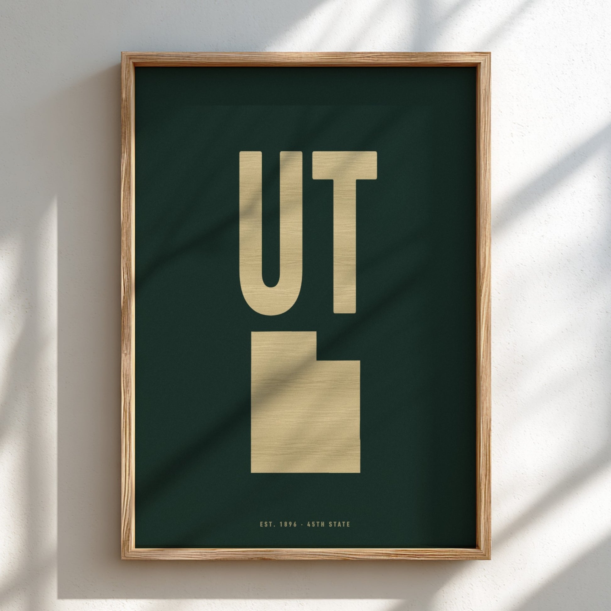 Framed poster with 'UT' in gold on a dark green background, leaning against a light wall.