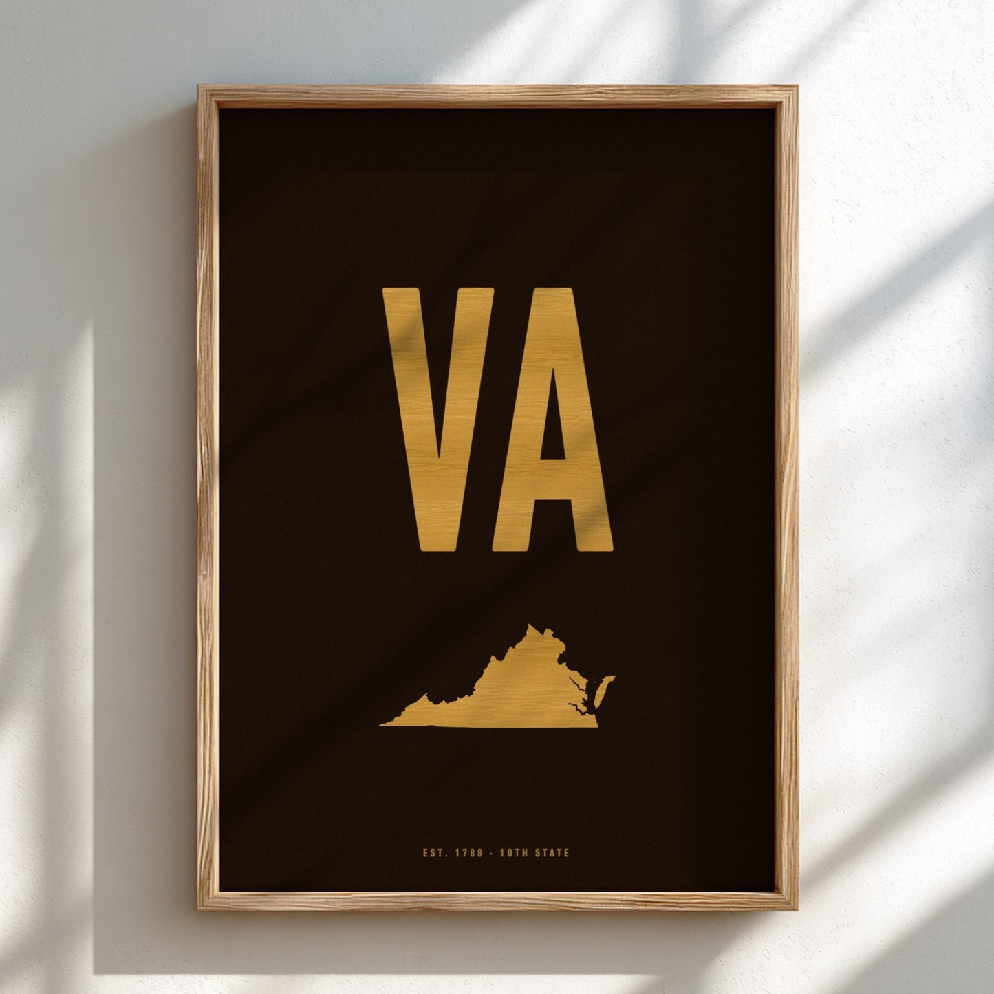 Framed poster with 'VA' in gold on a black background, featuring a map of Virginia, against a light wall.