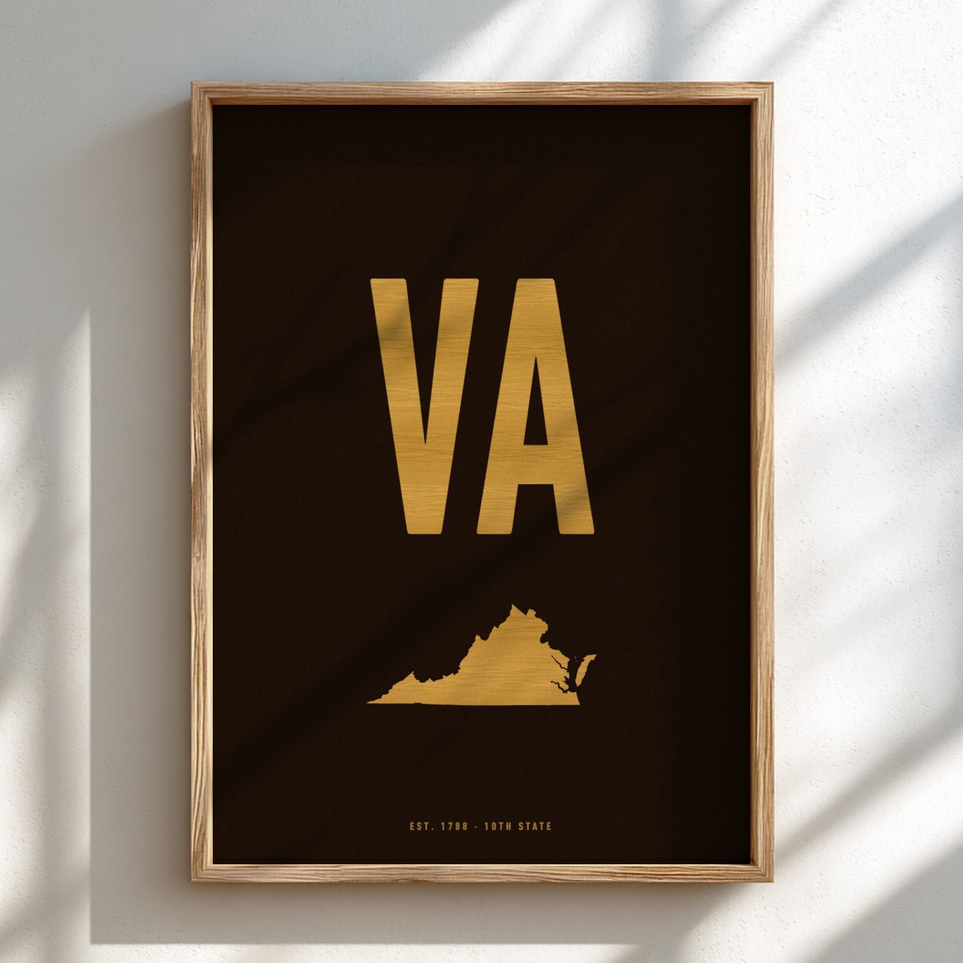 Framed poster with 'VA' in gold on a black background, featuring a map of Virginia, against a light wall.