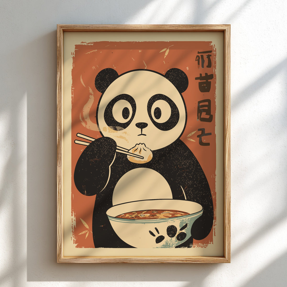 A framed art print featuring a retro-style panda eating dumplings from a bowl, mounted on a white wall with soft diagonal shadows.