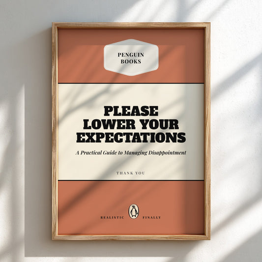 Framed book cover with 'Please Lower Your Expectations' text on a white wall.