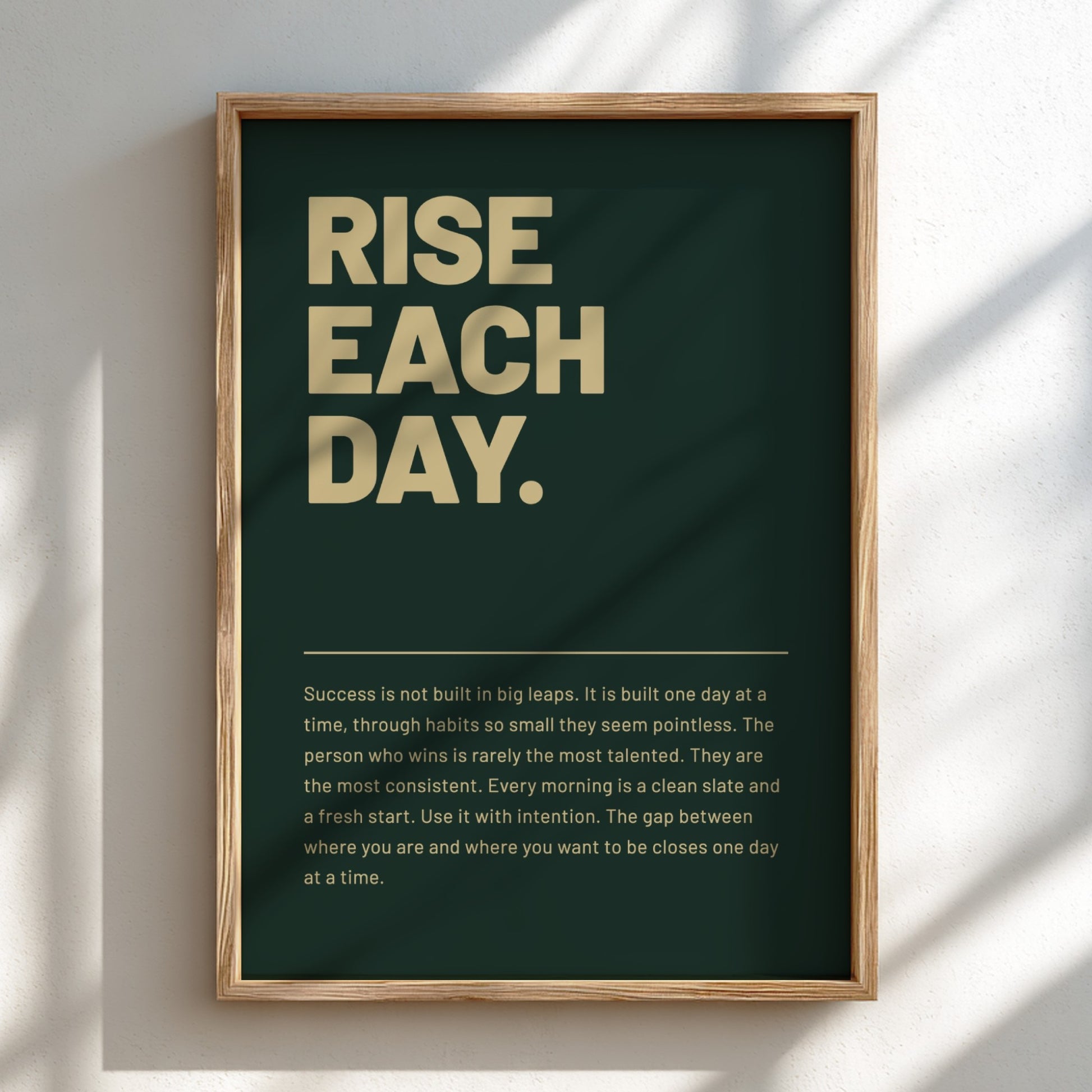 Framed poster with motivational quote 'RISE EACH DAY.' on a dark green background.