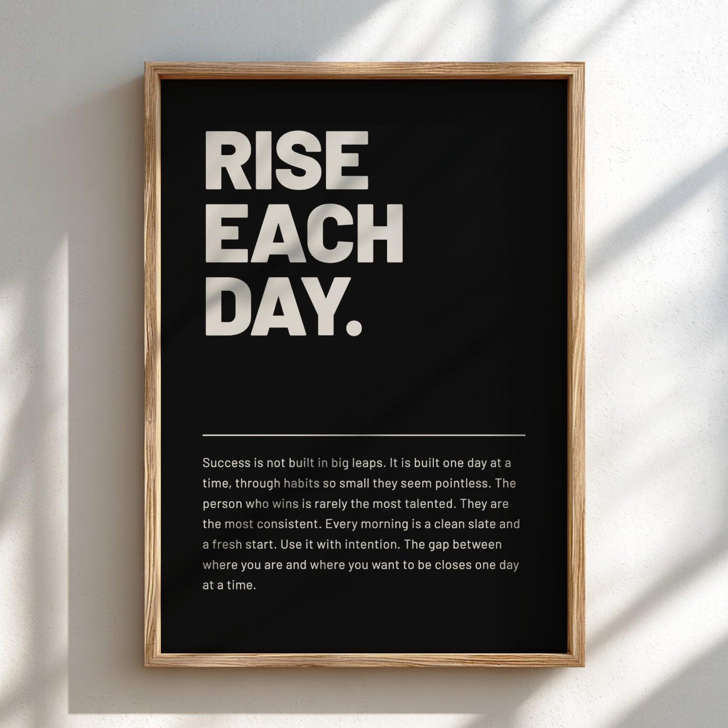 Framed poster with motivational quote 'RISE EACH DAY.' on a black background