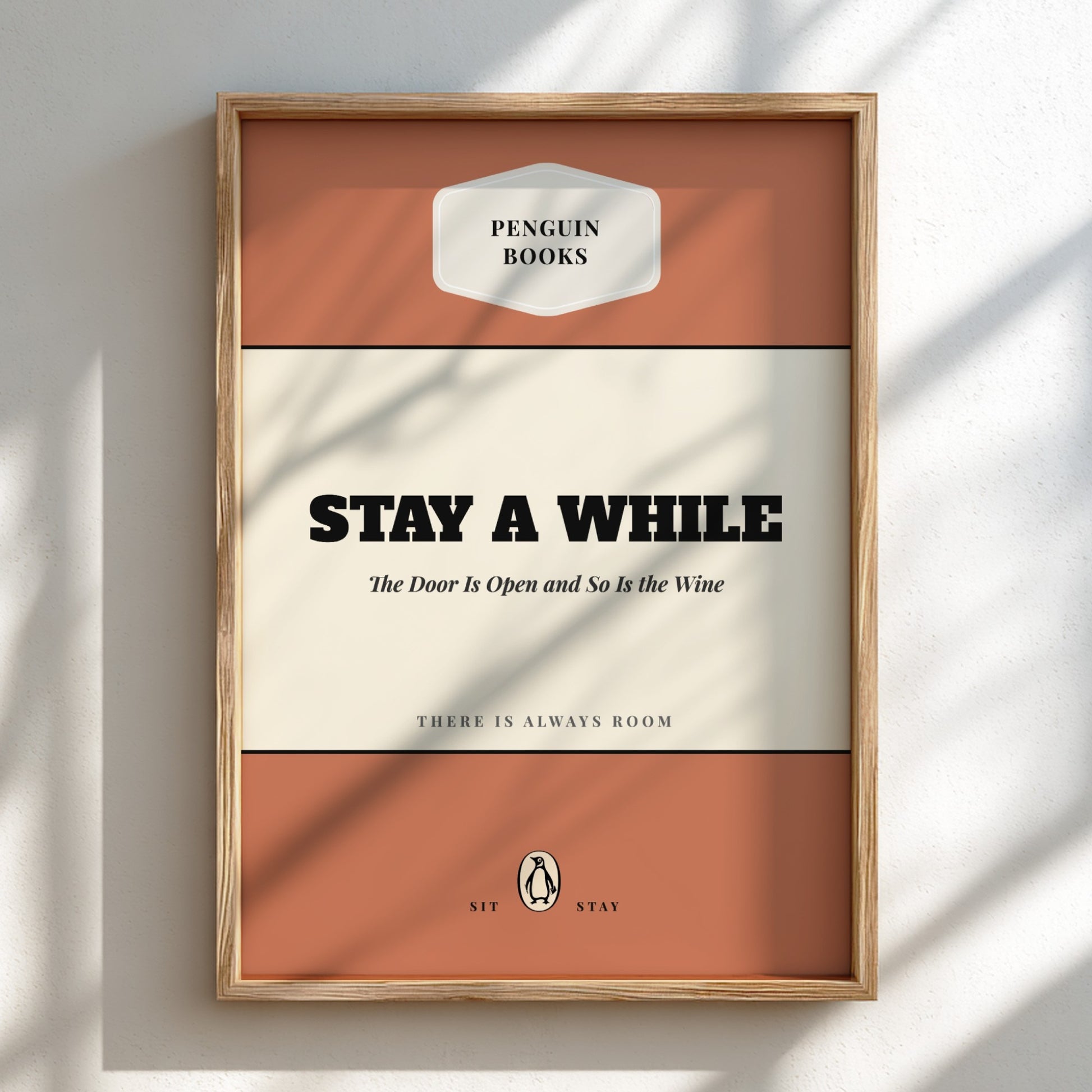 Framed Penguin Books poster with text 'Stay a While' on a white wall.