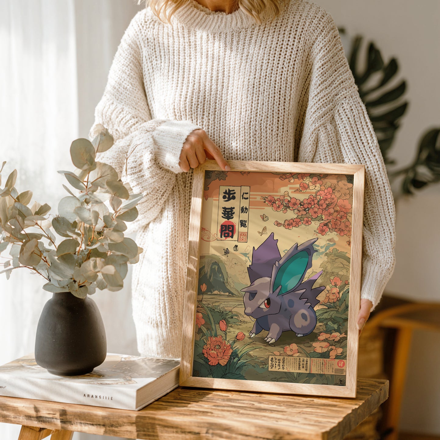 Person holding a framed illustration of Nidoran Pokemon in a decorative setting
