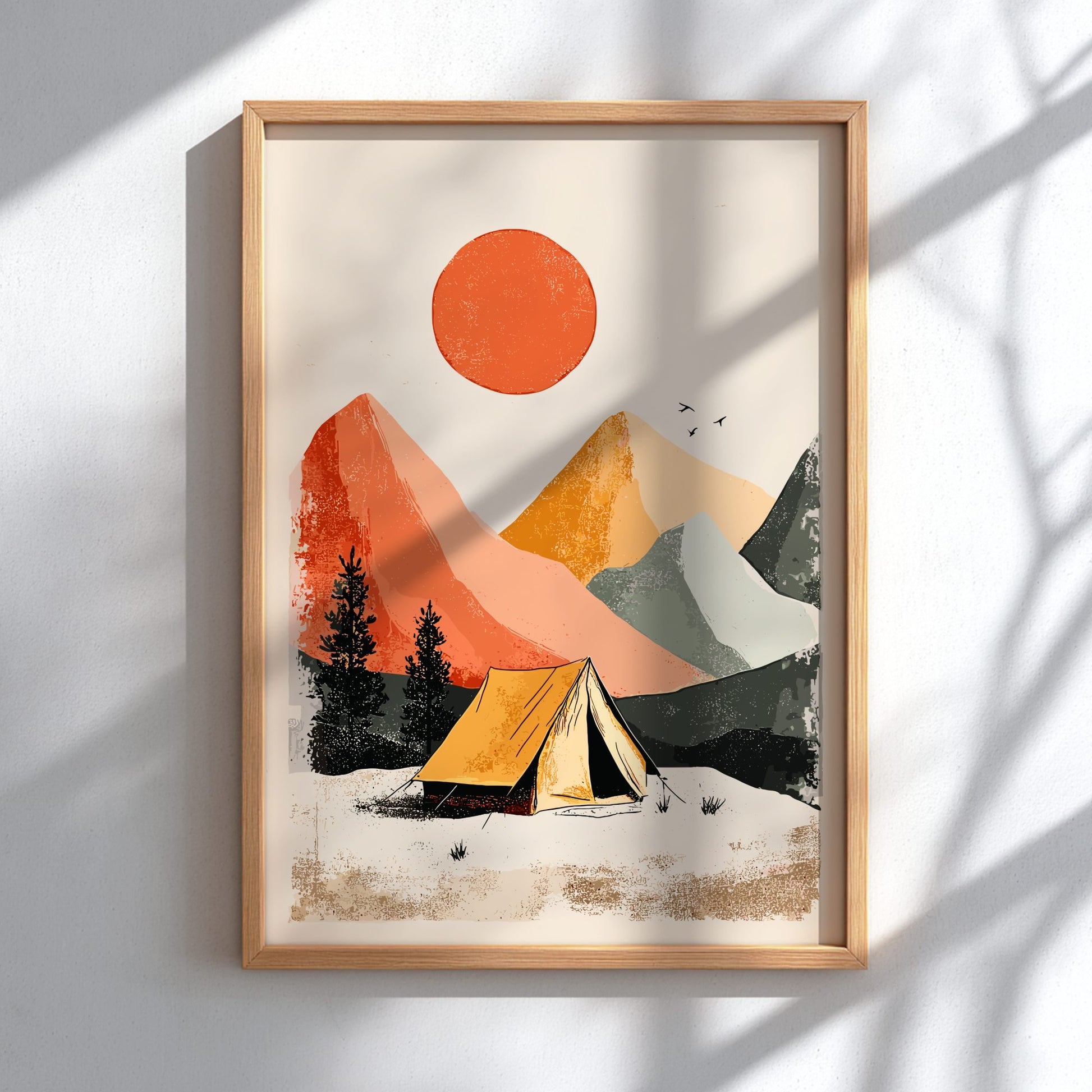 Framed artwork of a mountain landscape with a tent and orange sun on a white wall.