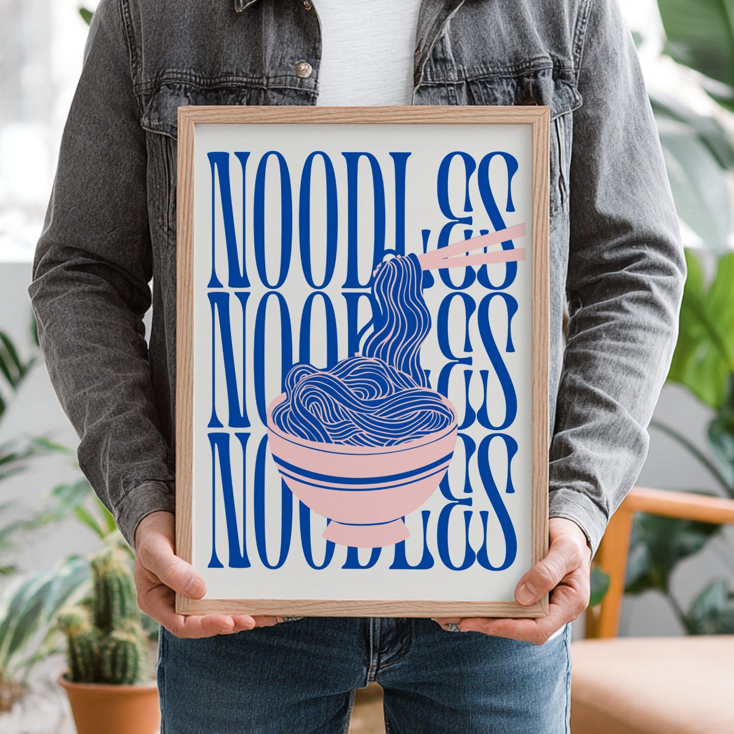 Person holding a framed artwork with 'Noodles' text and illustration.