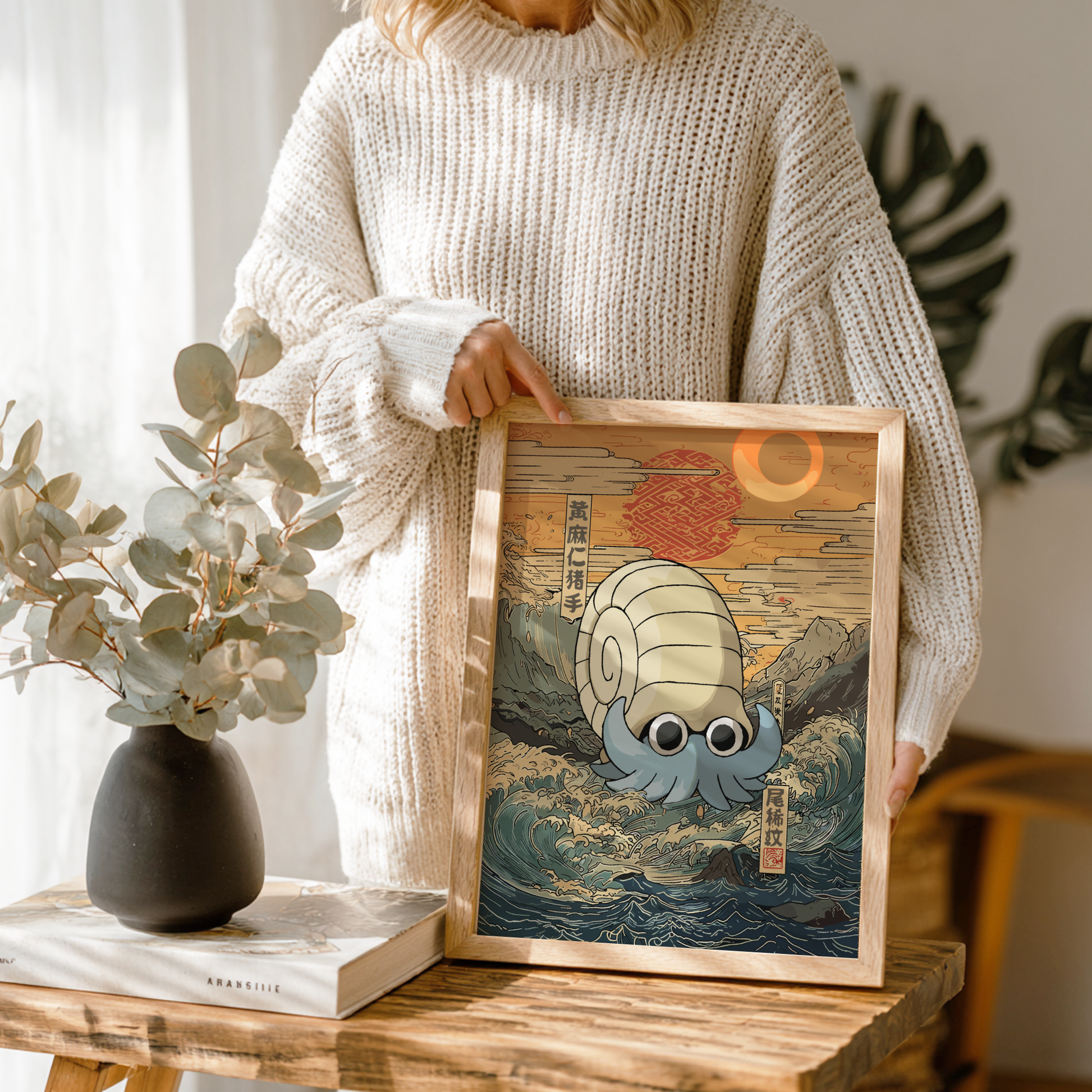 Person holding a framed artwork of Omanyte Pokemon on a wooden table with a vase and book in the background.