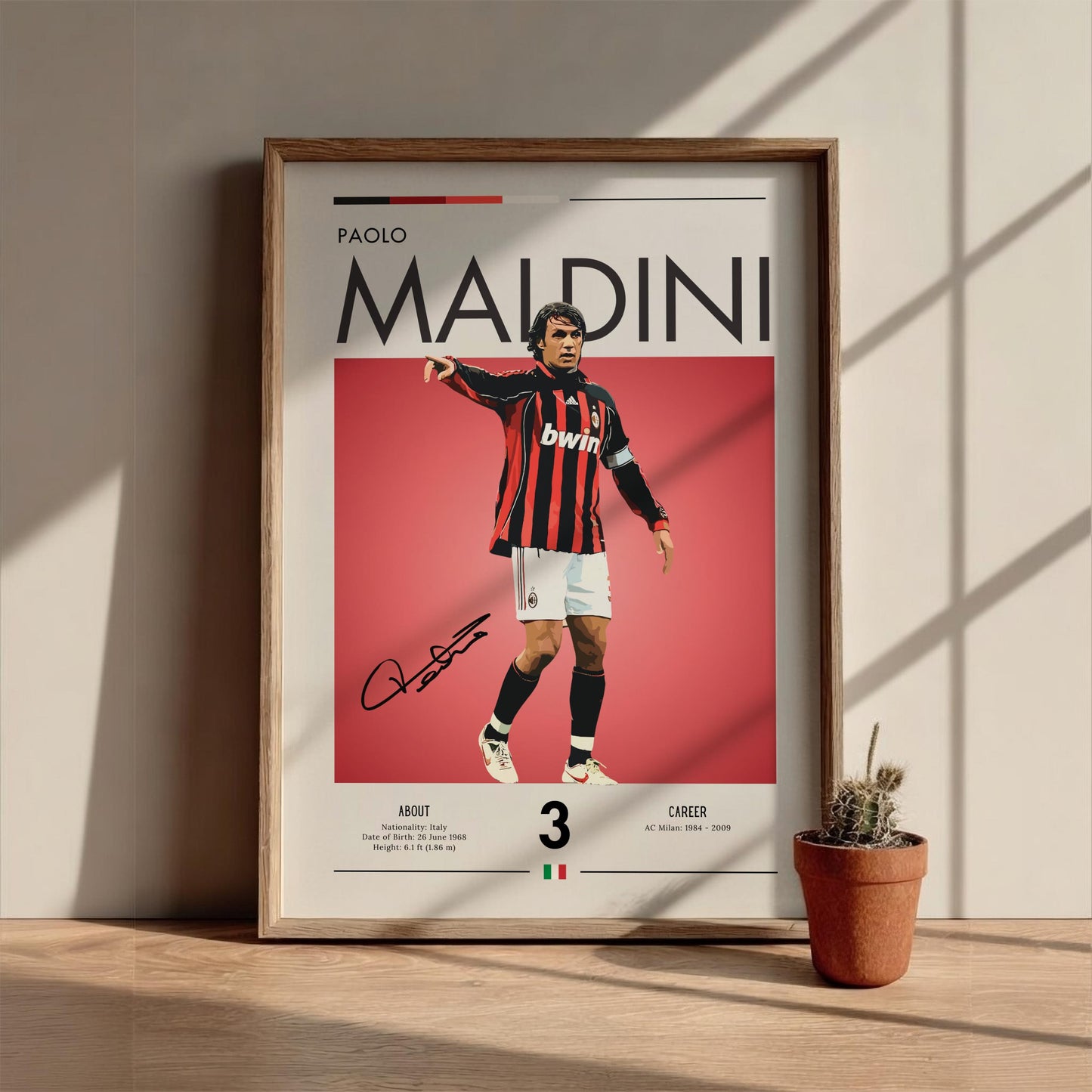 Framed poster of a soccer player with a red background, placed on a wooden surface with a plant.