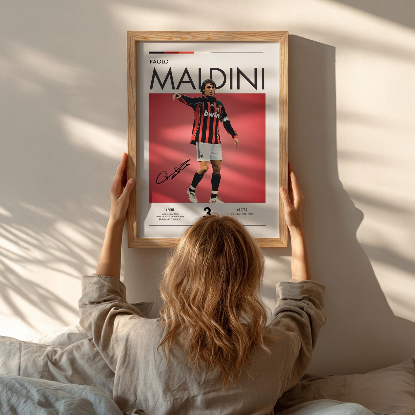 Person hanging a framed poster of Paolo Maldini on a wall