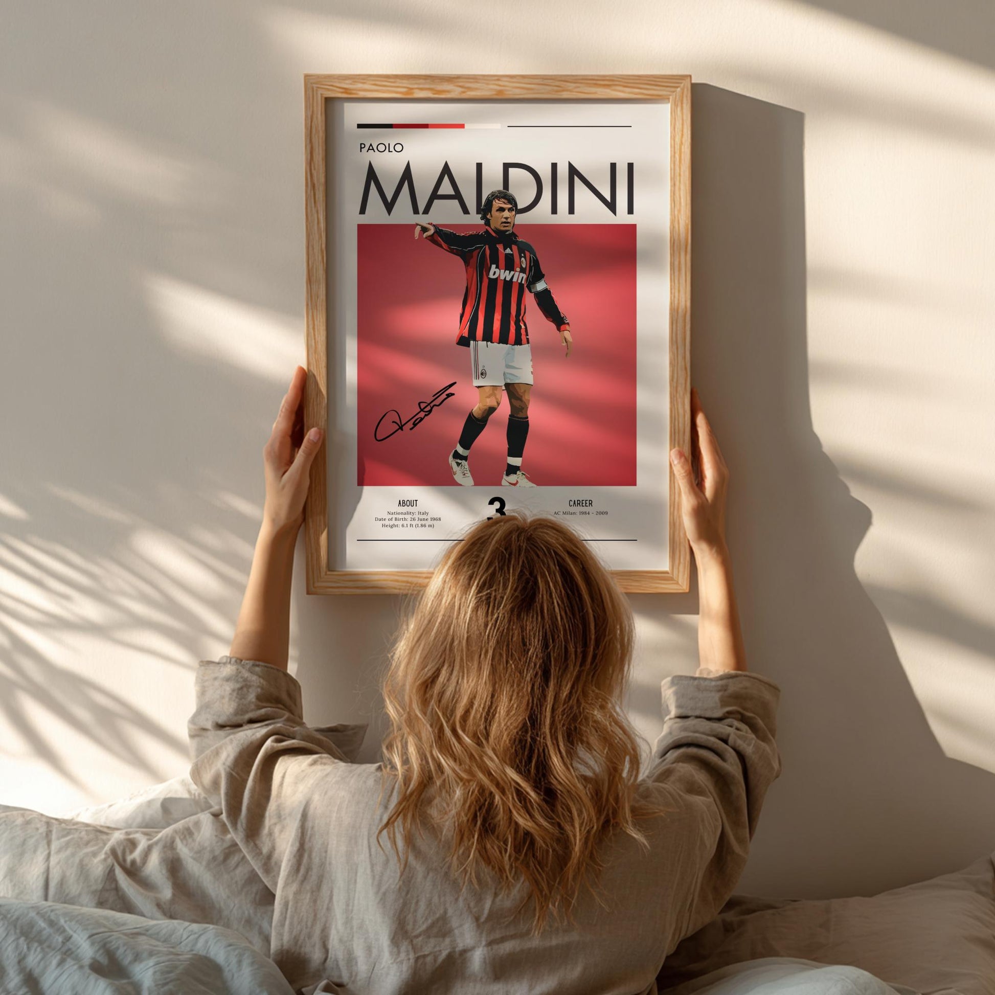 Person hanging a framed poster of Paolo Maldini on a wall
