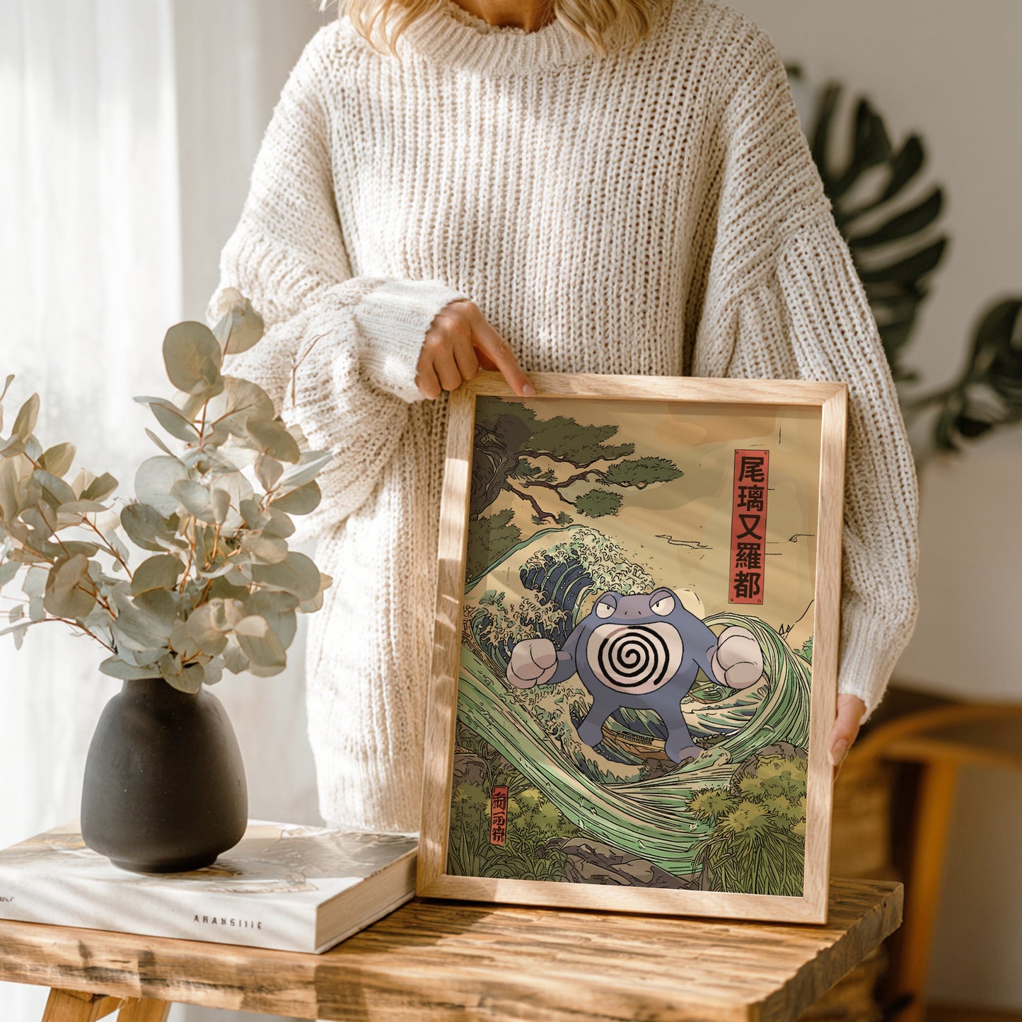 Person holding a framed artwork of a stylized Poliwrath Pokemon design, in a home setting.