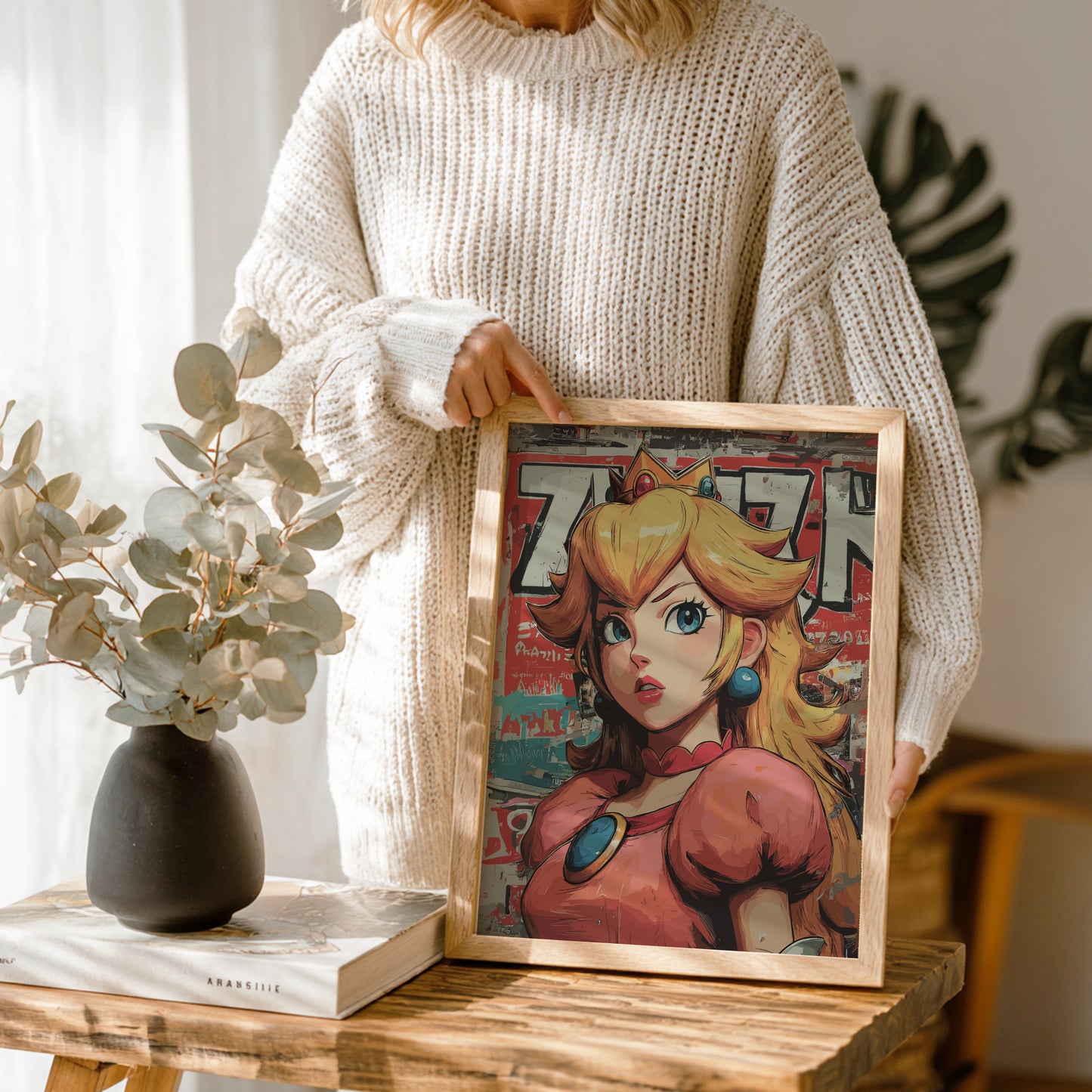 Person holding a framed illustration of Princess Peach on a wooden table.
