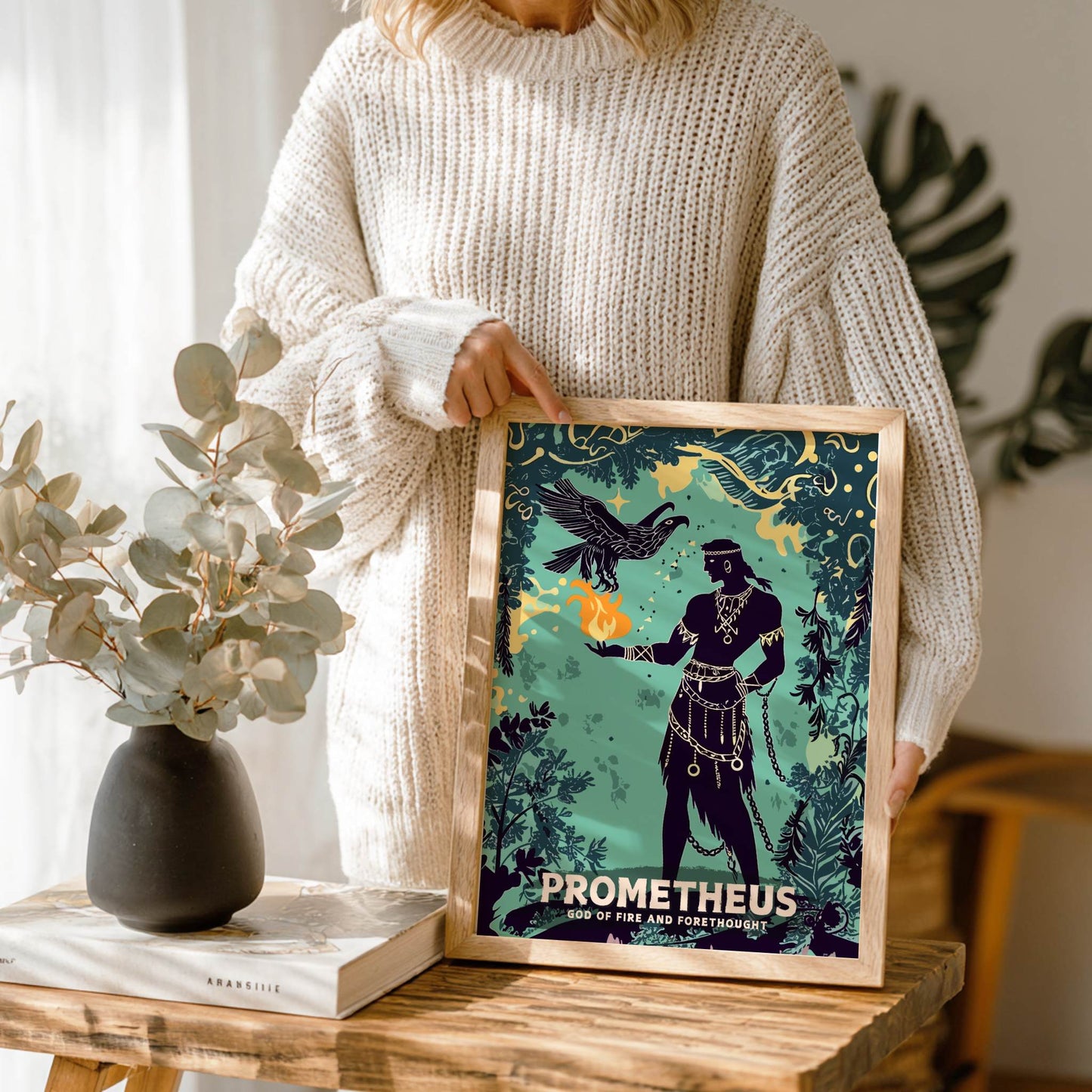 Person holding a framed 'Prometheus' poster on a wooden table with decor items.