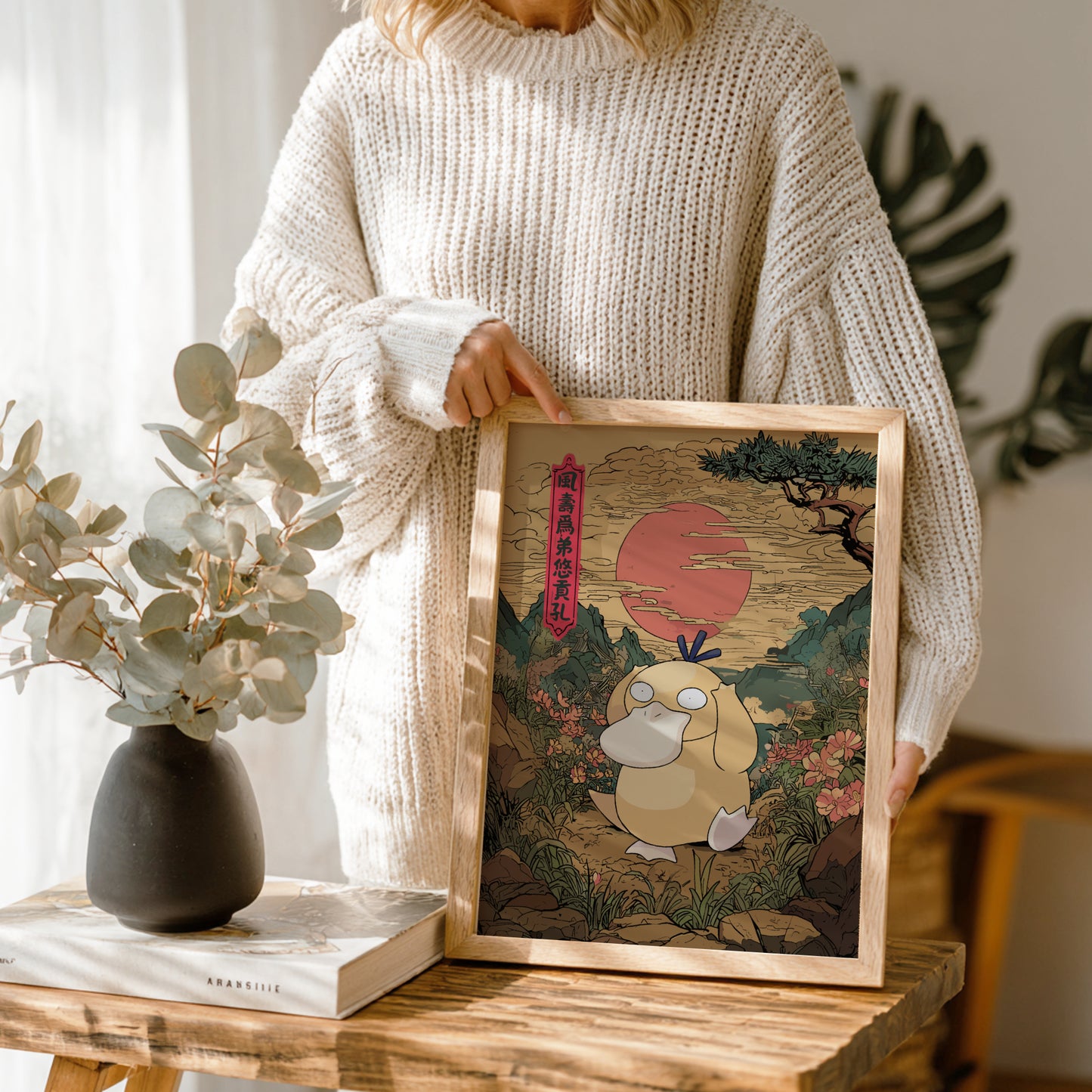 Person holding a framed artwork of Psyduck Pokémon character with a scenic background