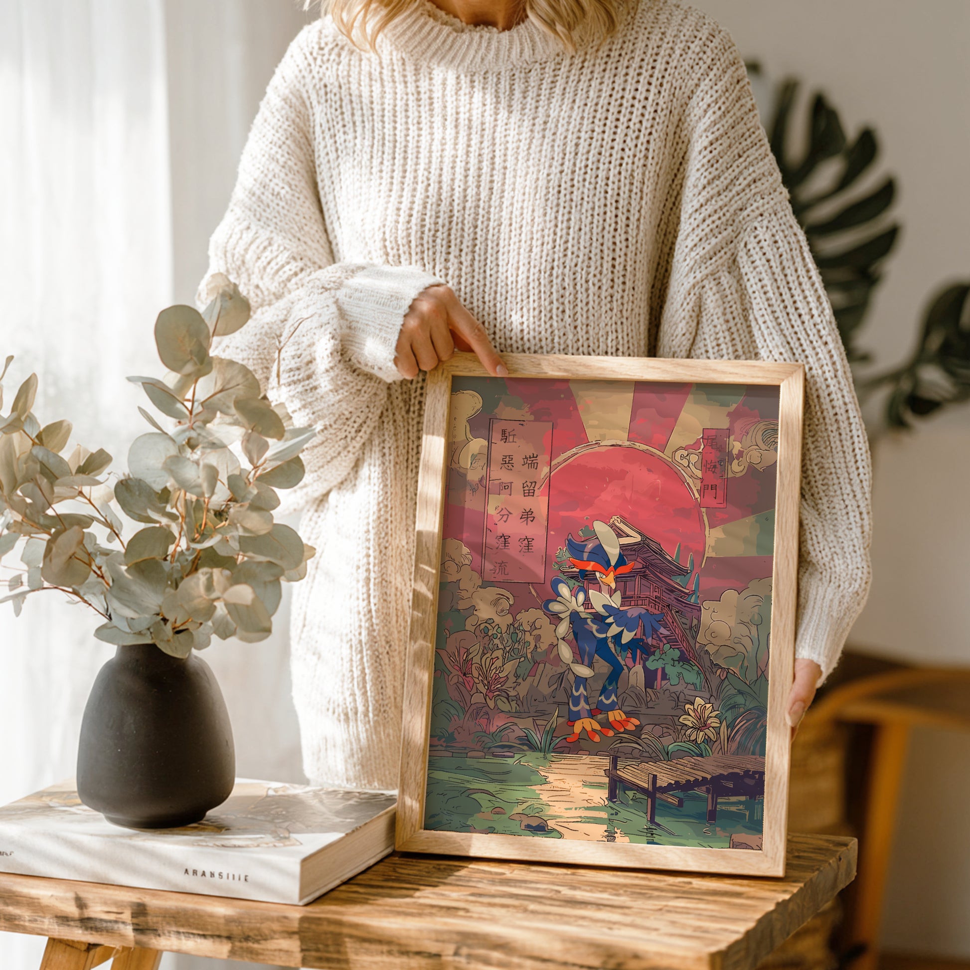 Person holding a framed artwork of Quaquaval Pokemon on a wooden table with a vase and book in the background.