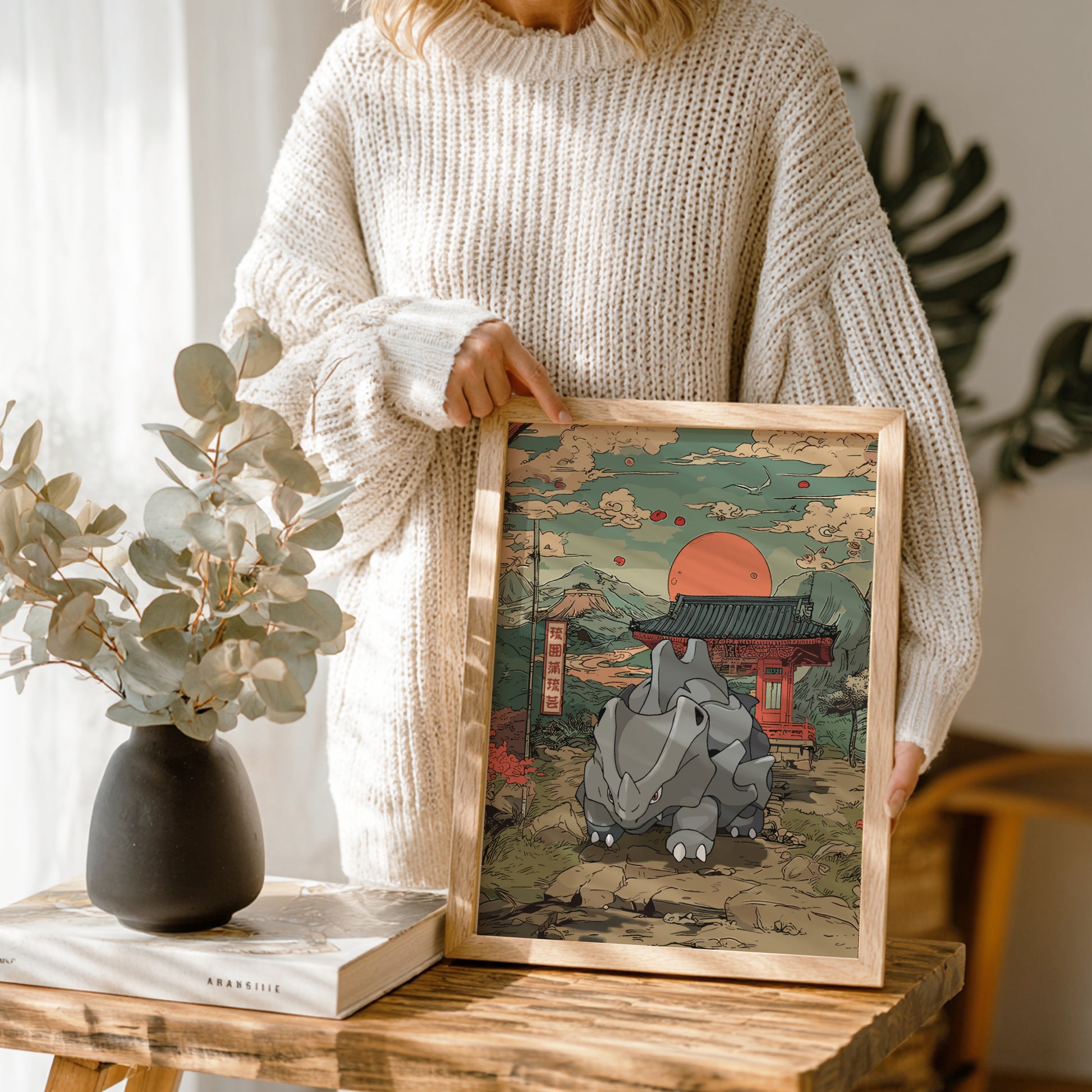 Person holding a framed artwork of Rhyhorn Pokemon in a traditional setting on a wooden table.