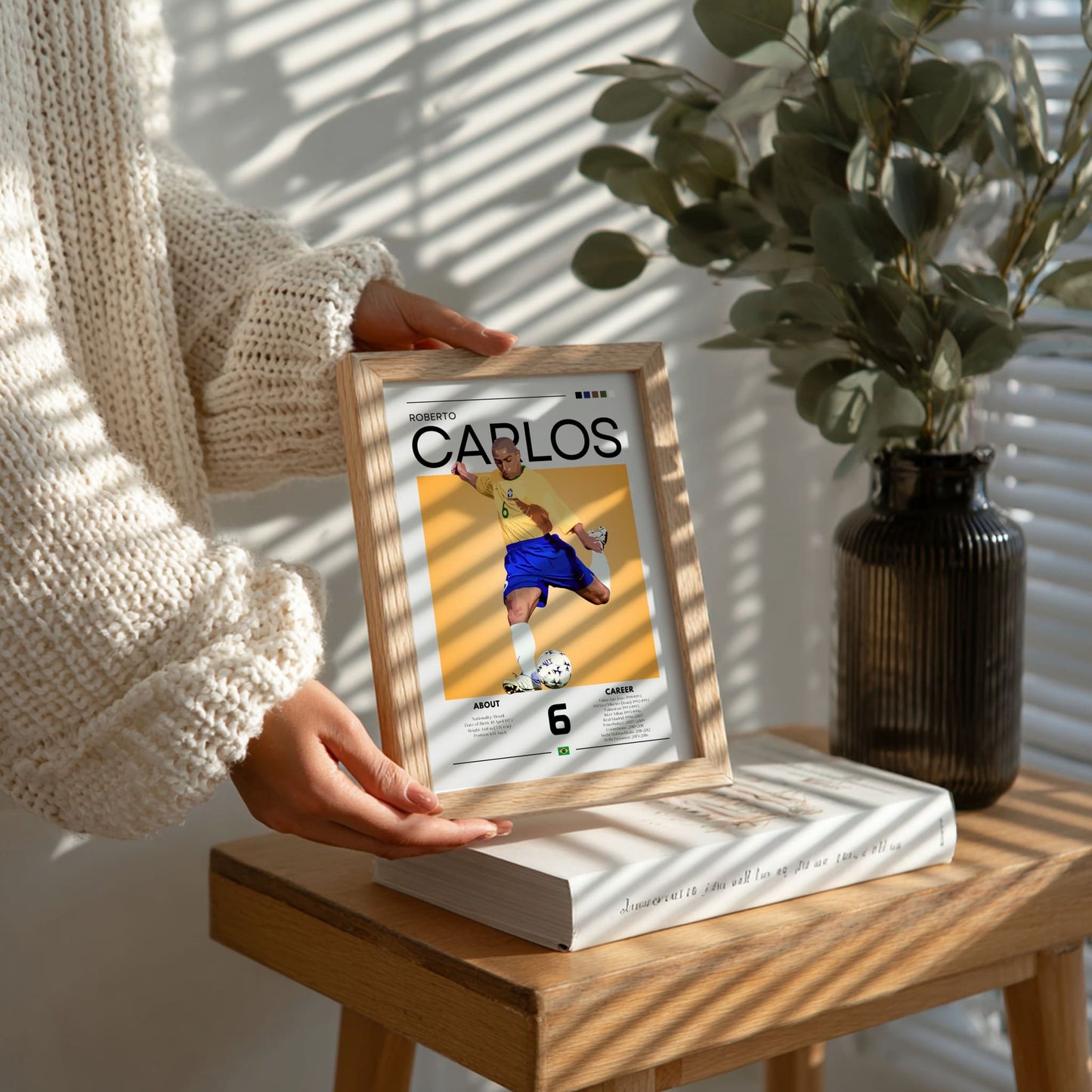 Person holding a framed picture of a soccer player on a wooden table with a plant in the background
