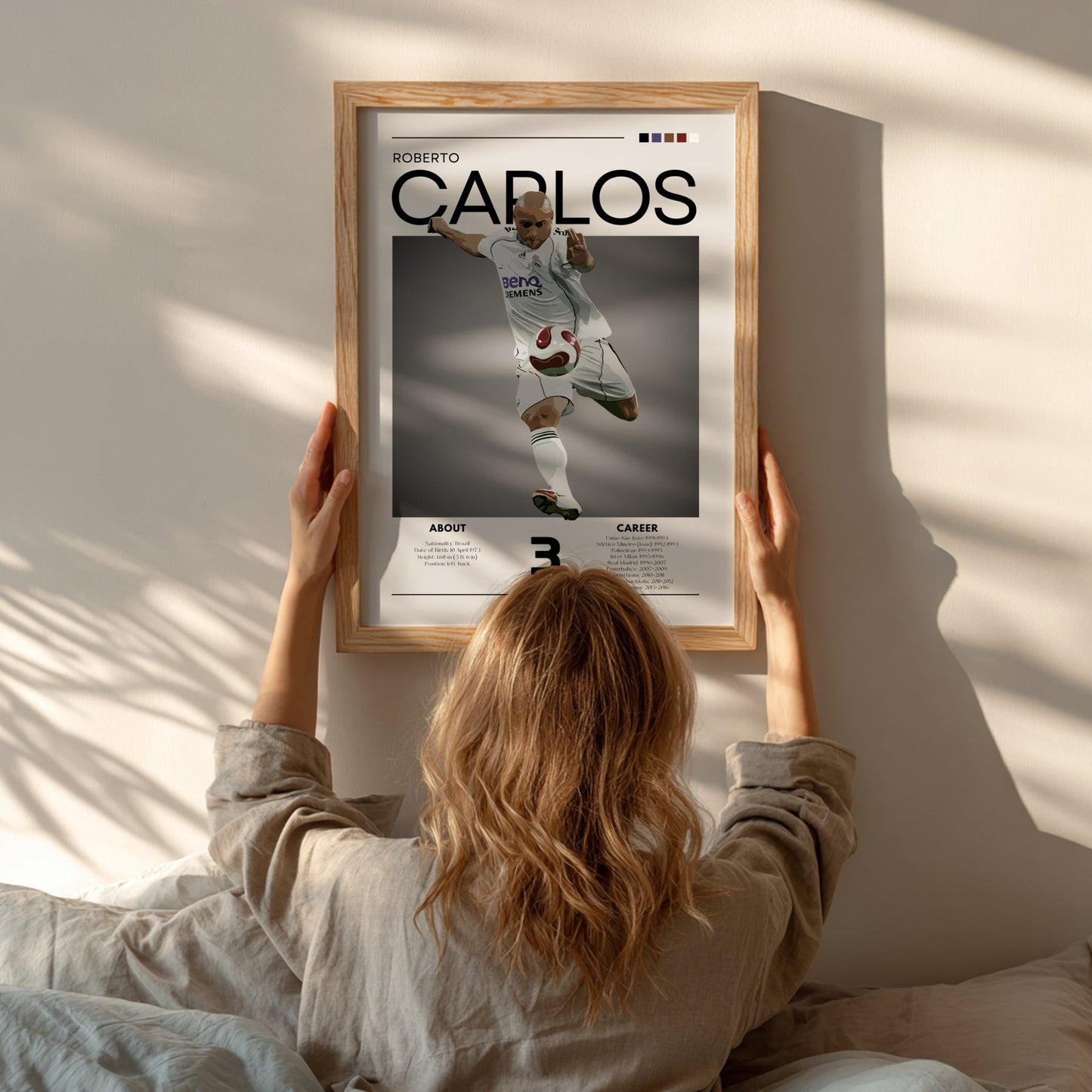 Person hanging a framed poster of Roberto Carlos on a wall