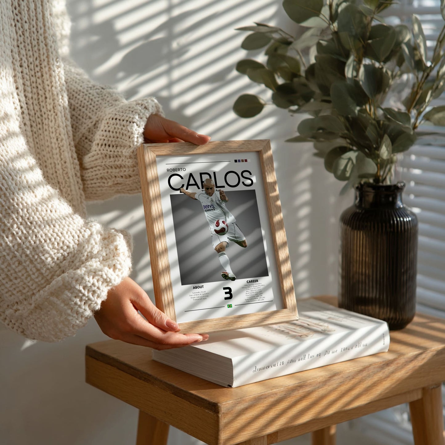 Person holding a framed picture of a soccer player on a wooden table with a plant in the background
