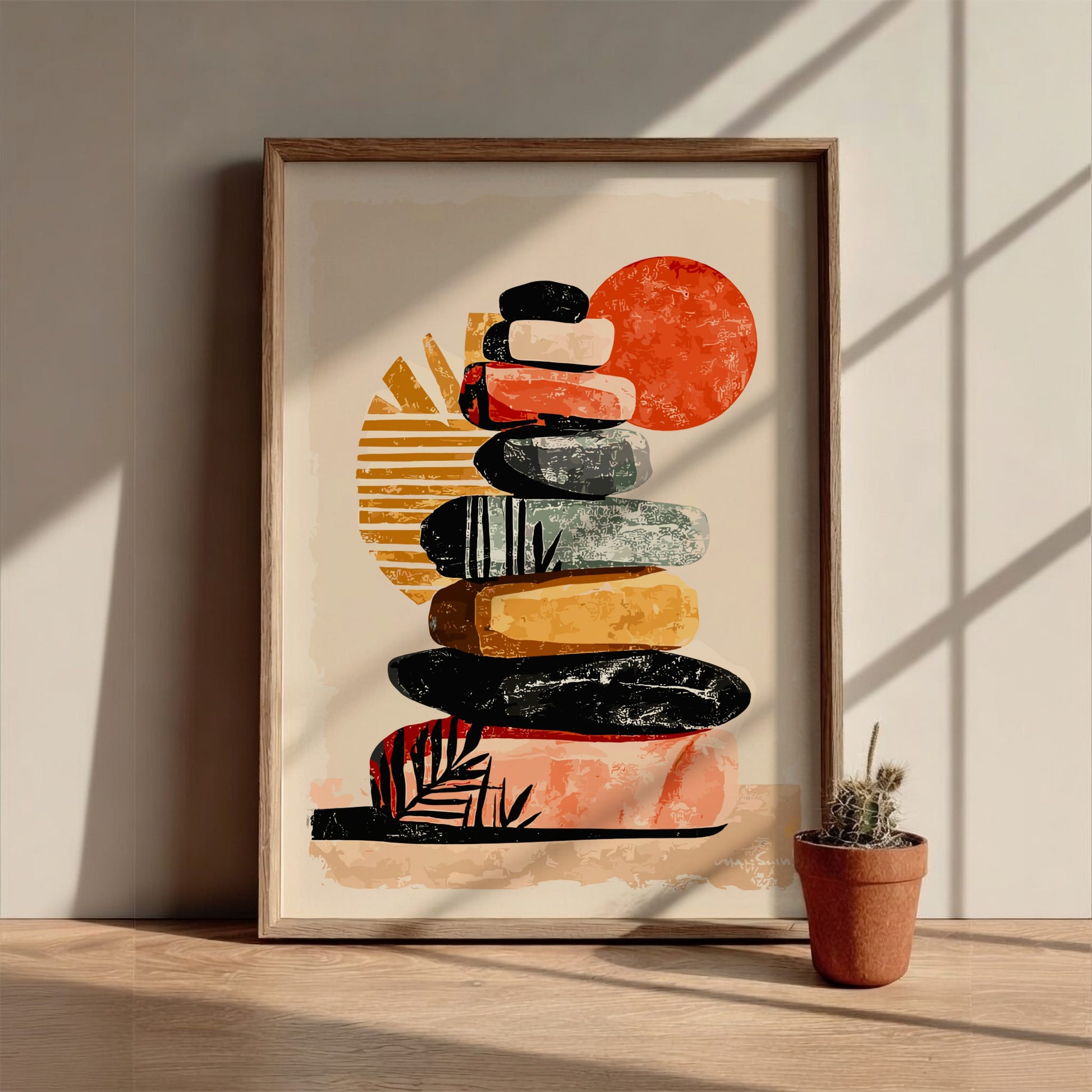Framed abstract art print of stacked stones with a potted plant on a wooden surface.