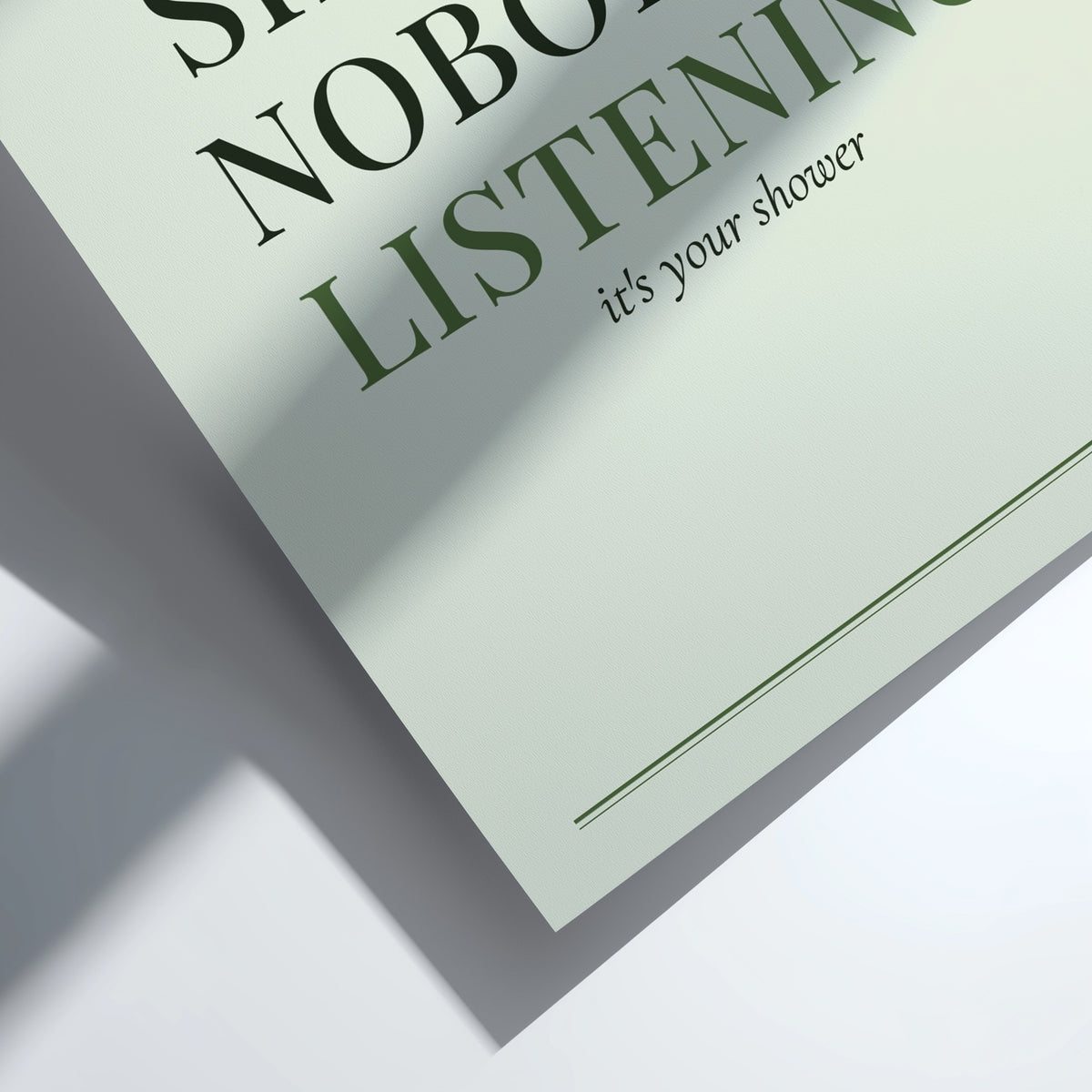 A close-up of a printed card or poster with the phrase 'LISTENING it's your shower' in dark green text on a pale mint background, photographed on a white surface with a strong diagonal shadow.