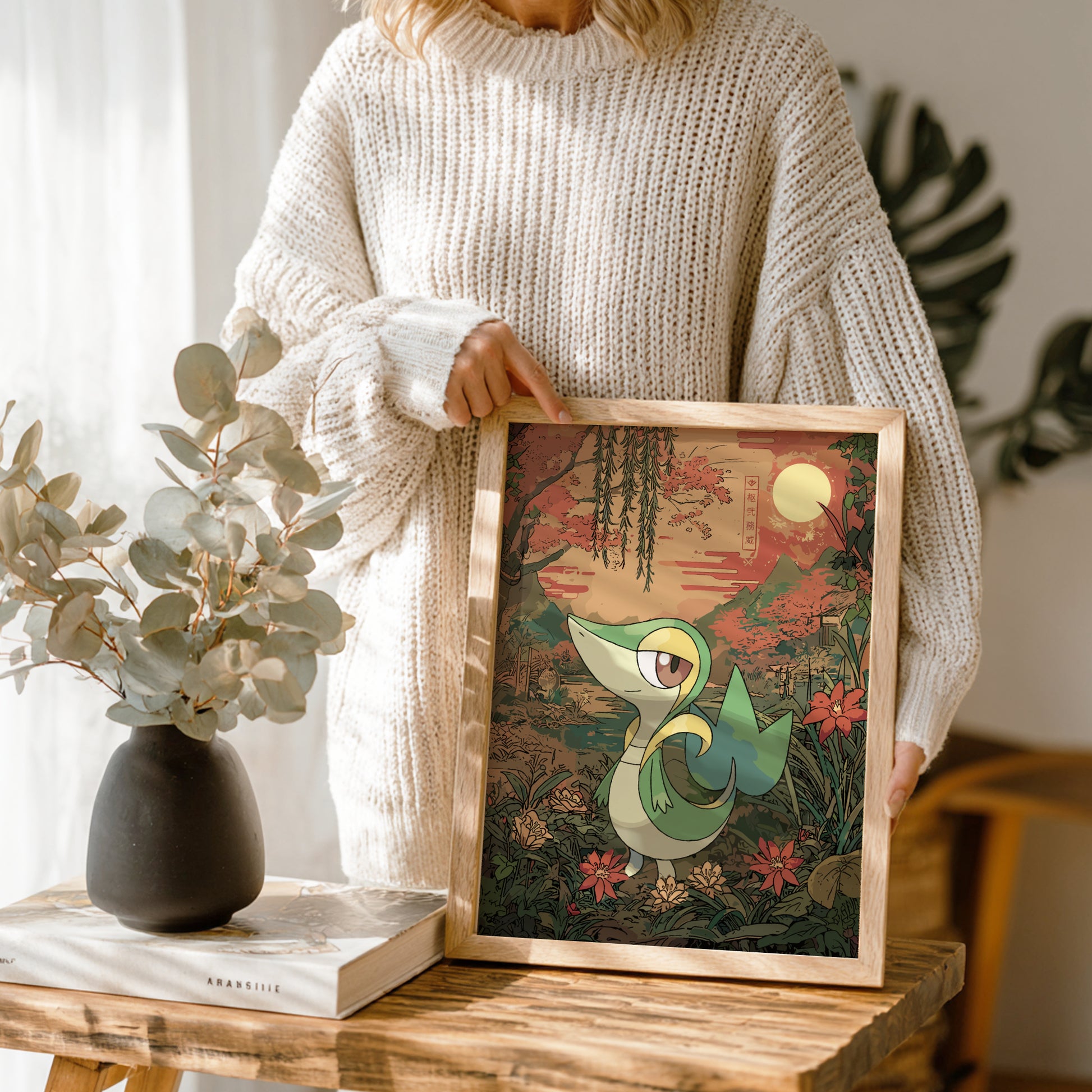 Person holding a framed illustration of Snivy Pokemon in a natural setting