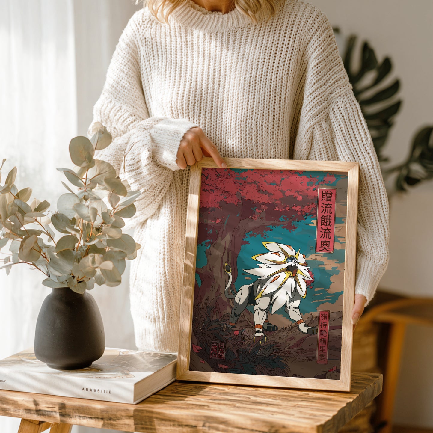 Person holding a framed artwork with a nature-themed design of Solgaleo Pokemon on a wooden table.