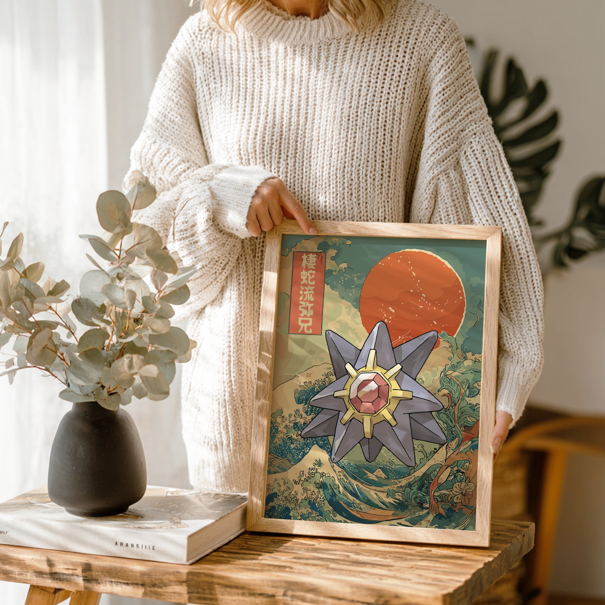 Person holding a framed artwork with a stylized Starmie Pokemon design in a home setting