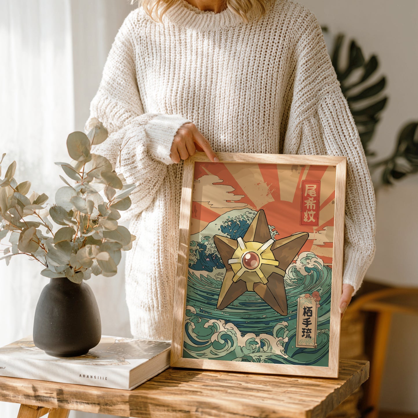 Person holding a framed artwork with a Staryu Pokemon design on a wooden table.