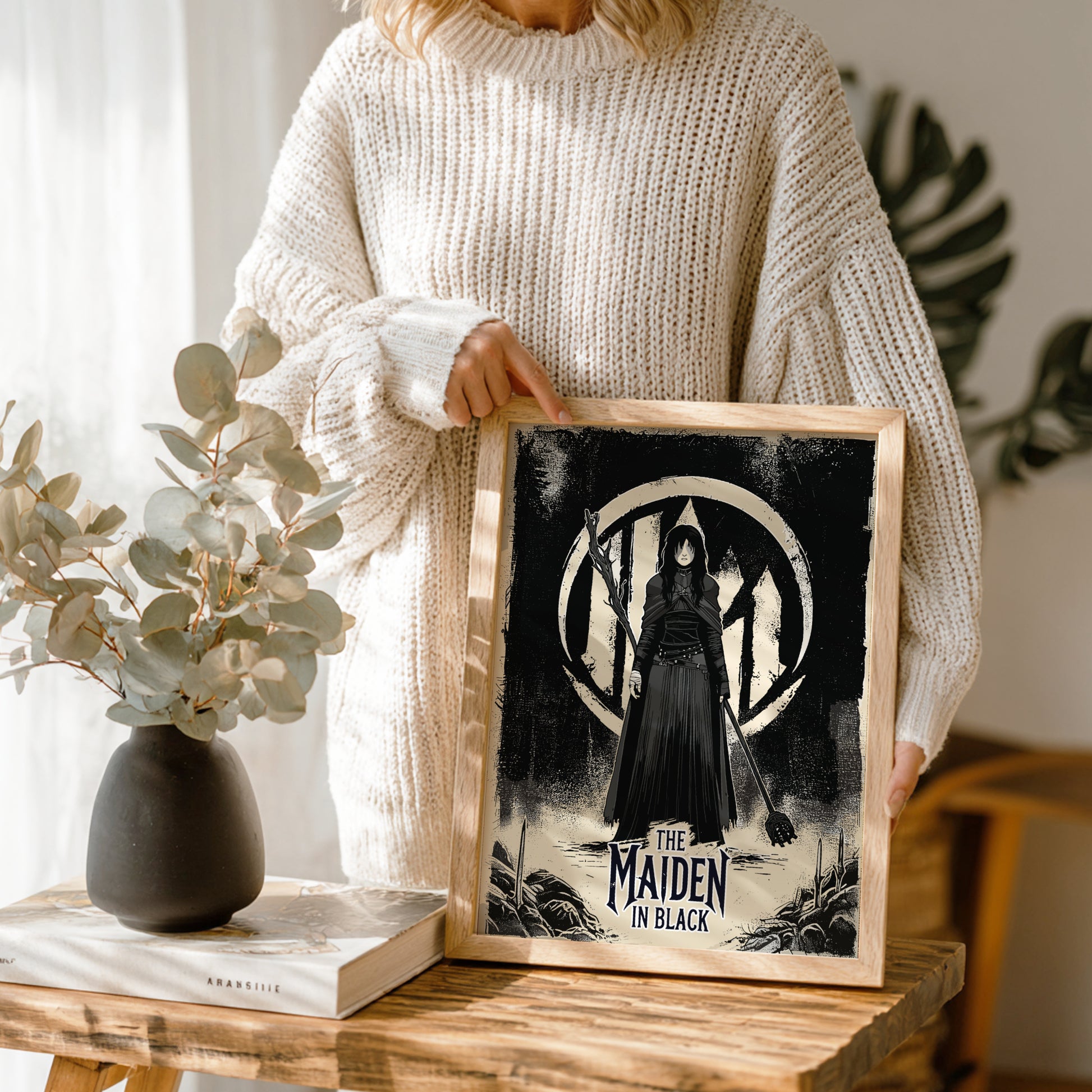 Person holding a framed artwork of The Maiden in Black from Dark Souls on a wooden table.