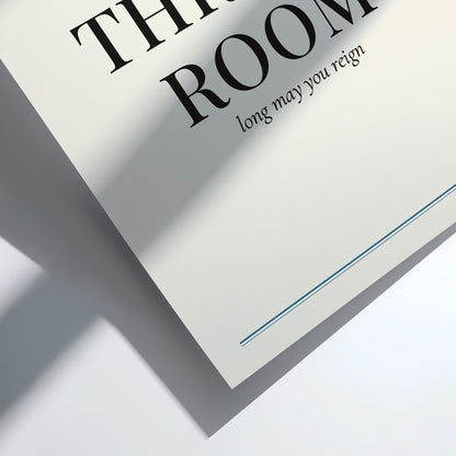 A close-up of a white printed card or page with large black serif text reading 'THY ROOM' and smaller text 'long may you reign,' plus a thin blue line near the bottom, photographed on a white surface with strong diagonal shadows.