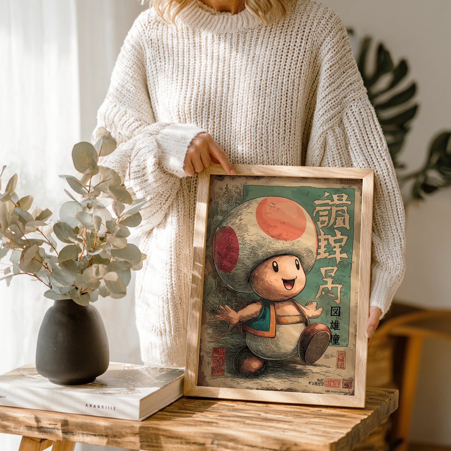 Person holding a framed illustration of Toad character on a wooden table.