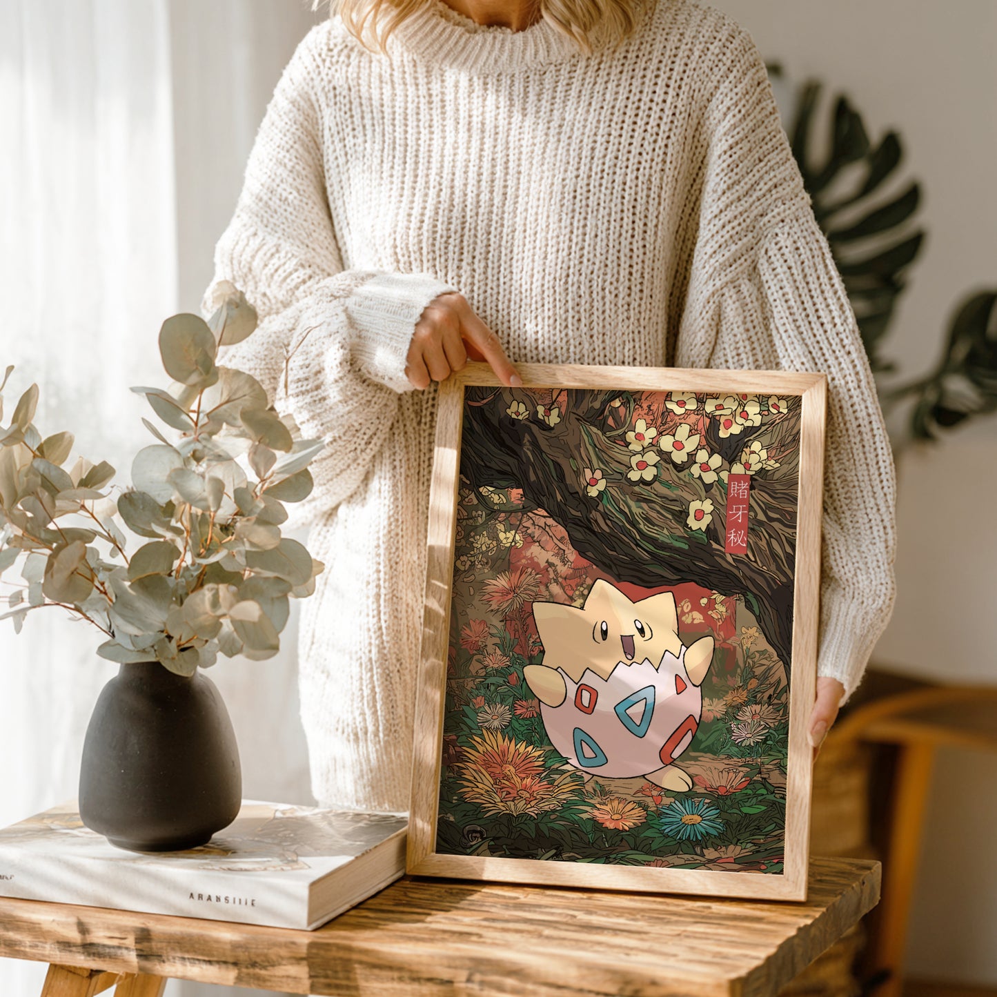 Person holding a framed artwork of Togepi Pokemon in a natural setting