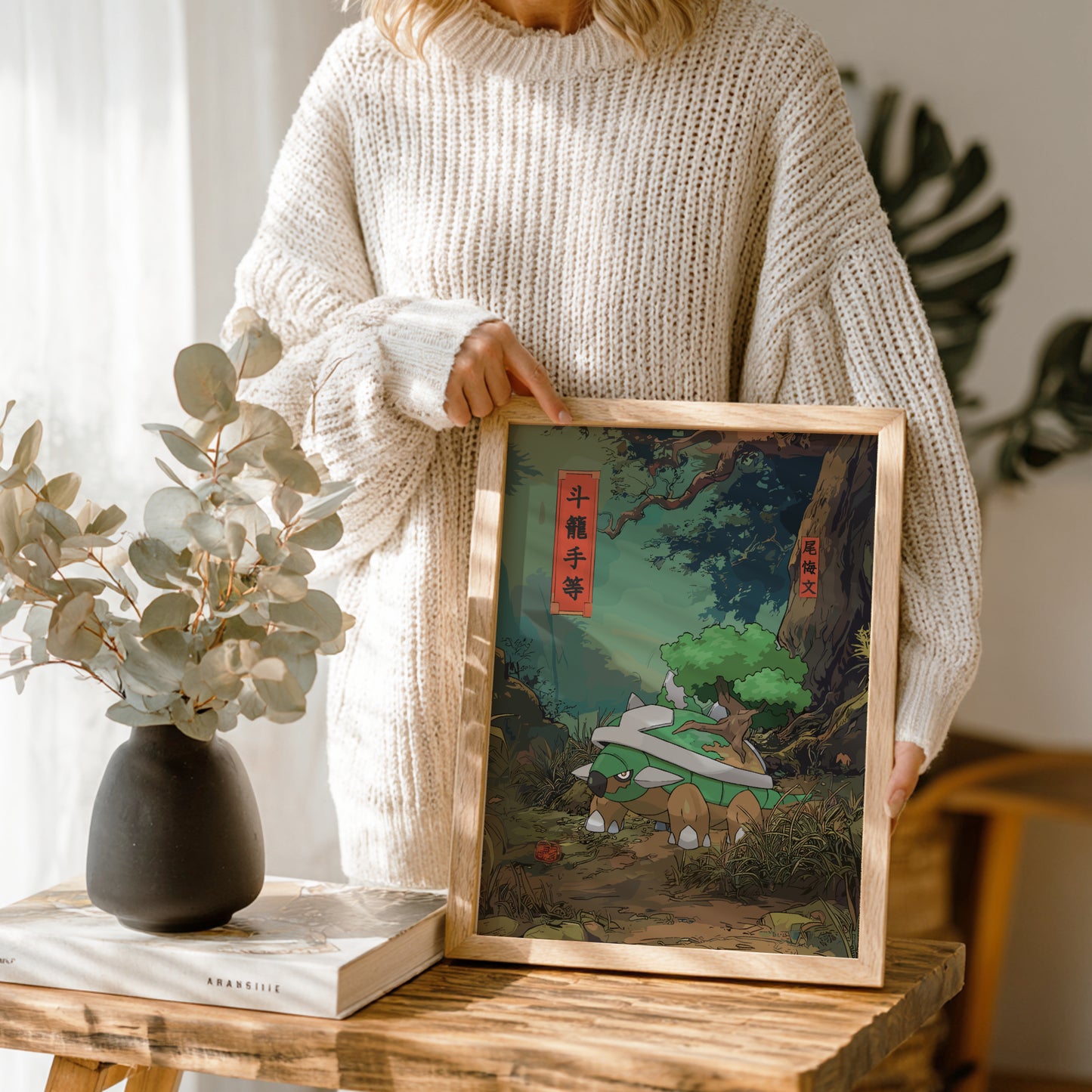 Person holding a framed artwork of a nature scene with Torterra Pokemon on a wooden table.