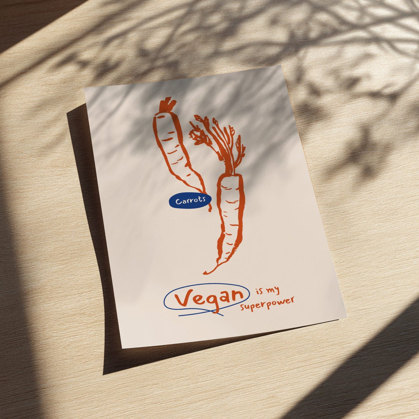Card with carrots illustration and 'Vegan is my superpower' text on a wooden surface