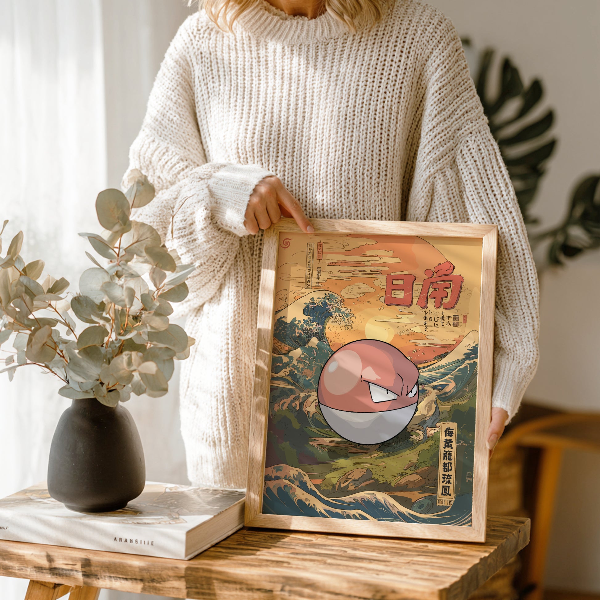 Person holding a framed artwork with a stylized Voltorb Pokemon design on a wooden table.